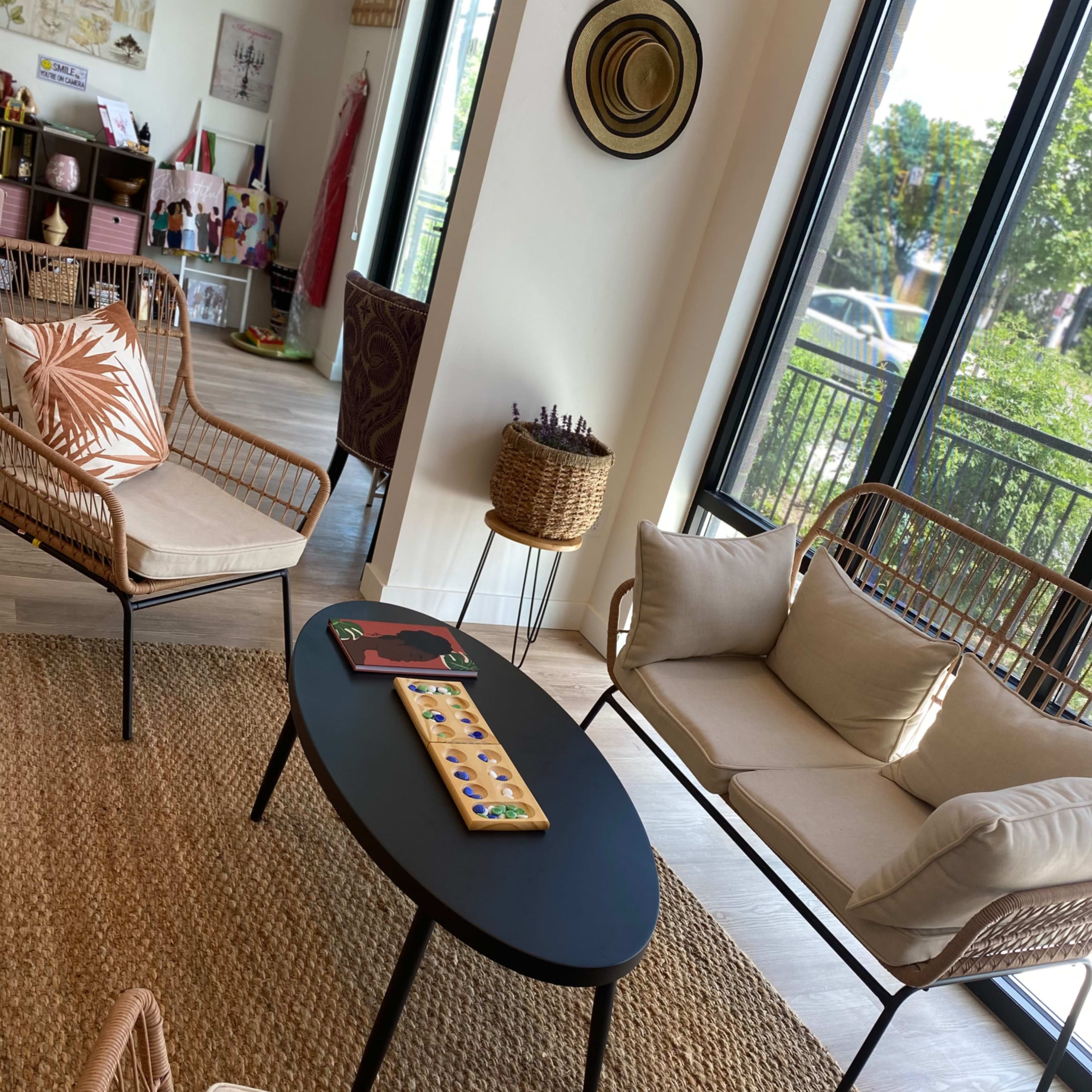 A modern living space with two woven chairs, a black oval coffee table, and large windows that let in natural light.