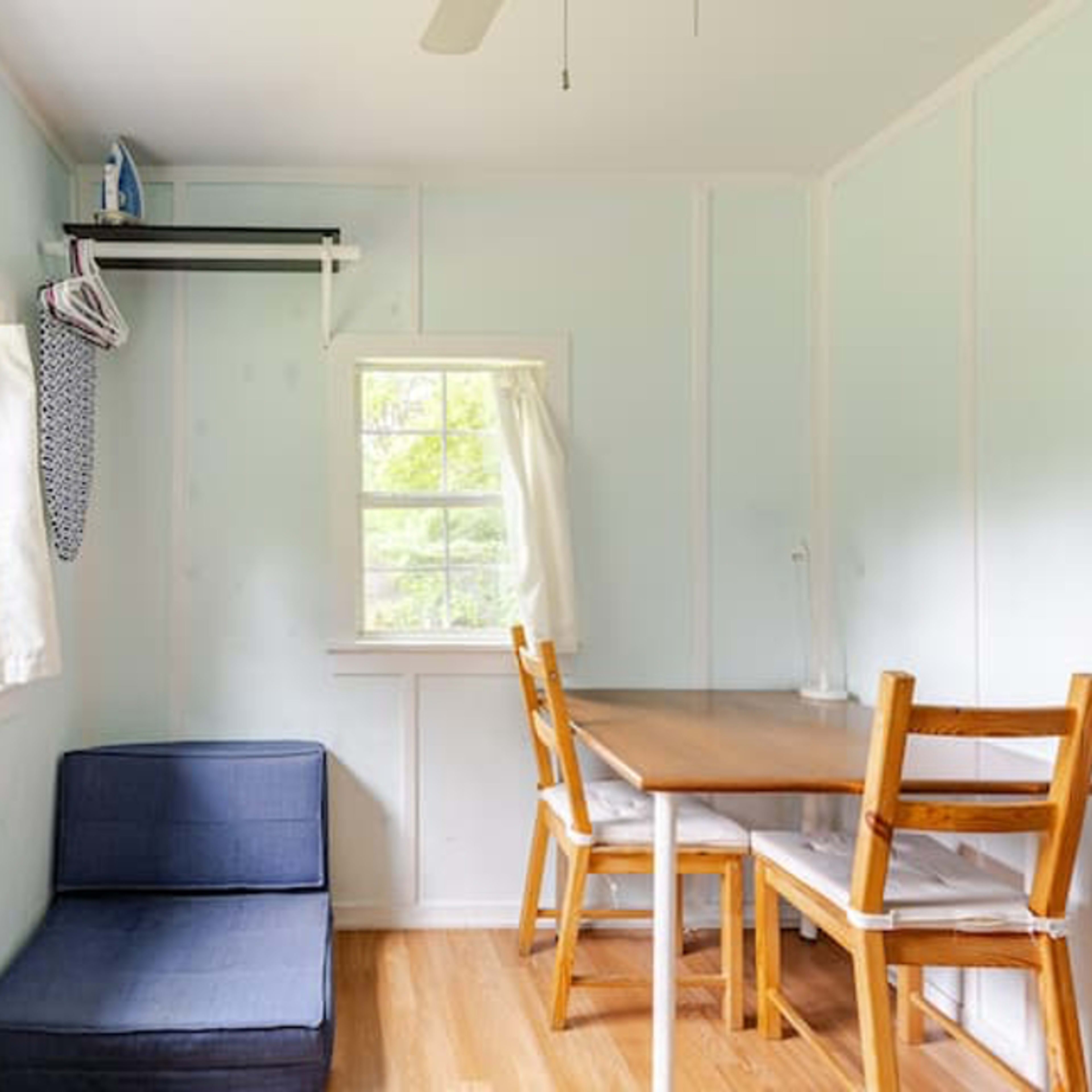 A light blue room with a small table and chairs near a window, along with a sofa against the wall.