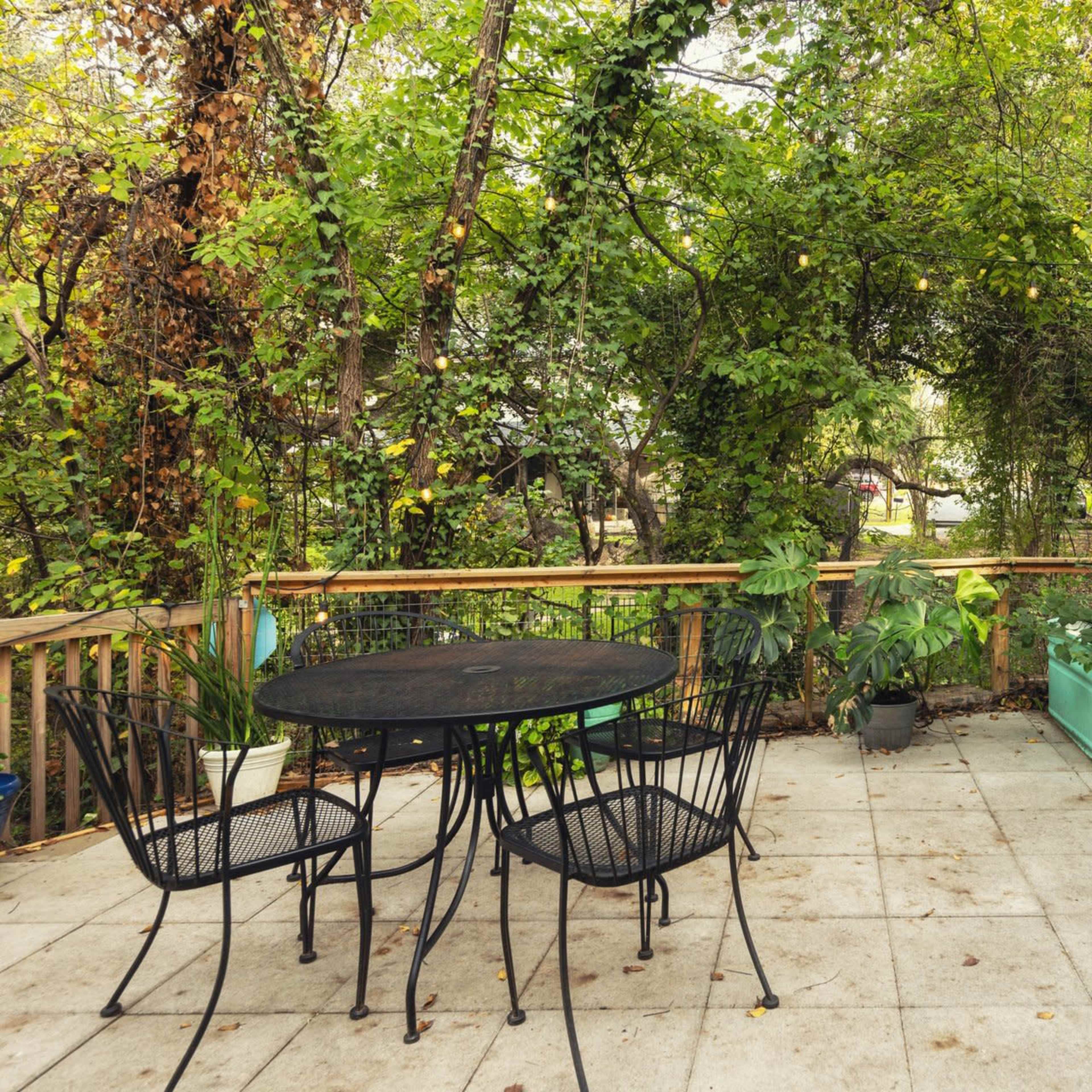An outdoor patio with a round table and four chairs surrounded by lush greenery and potted plants.