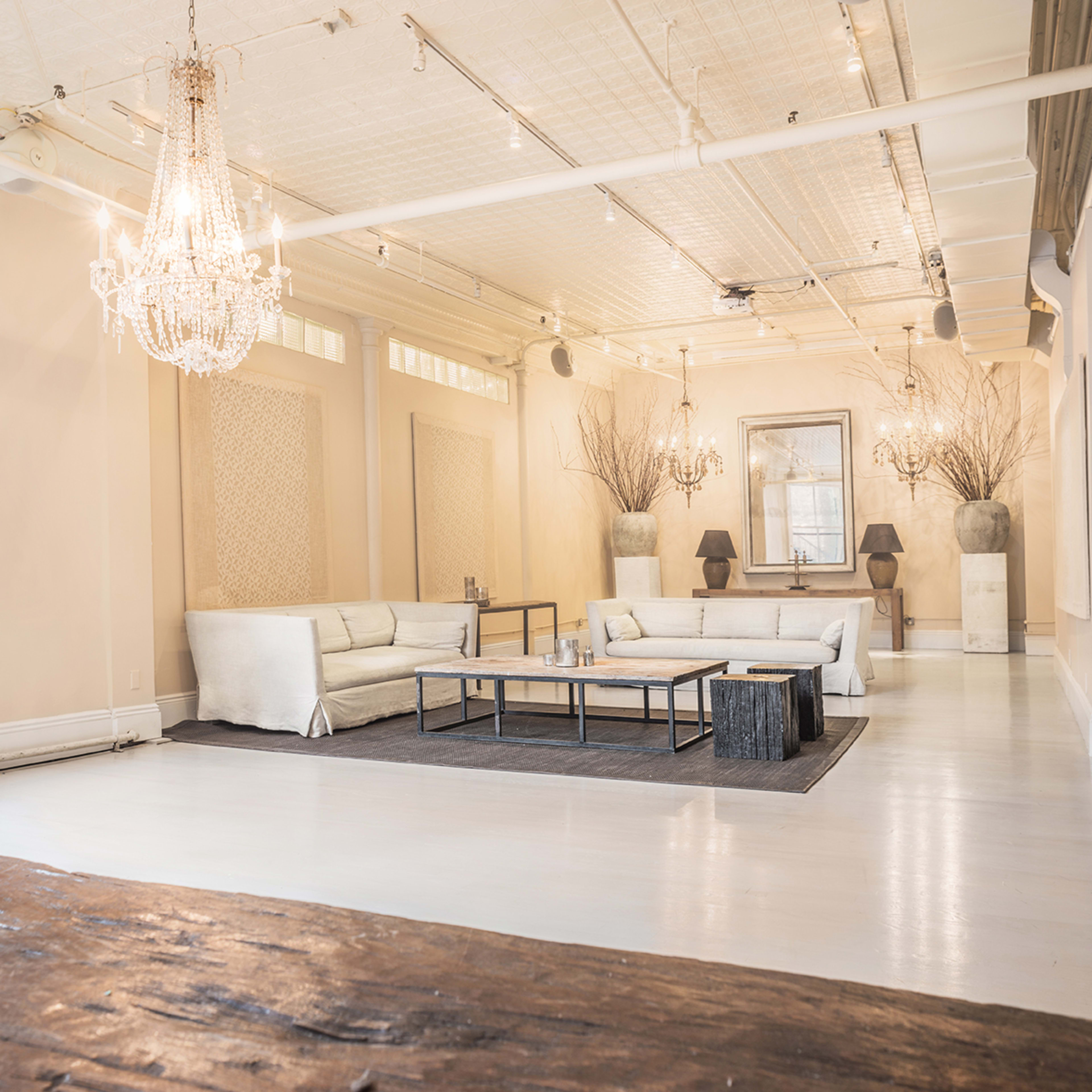 A spacious interior with light-colored walls, a central seating area featuring a white sofa set, a dark area rug, and elegant lighting fixtures.