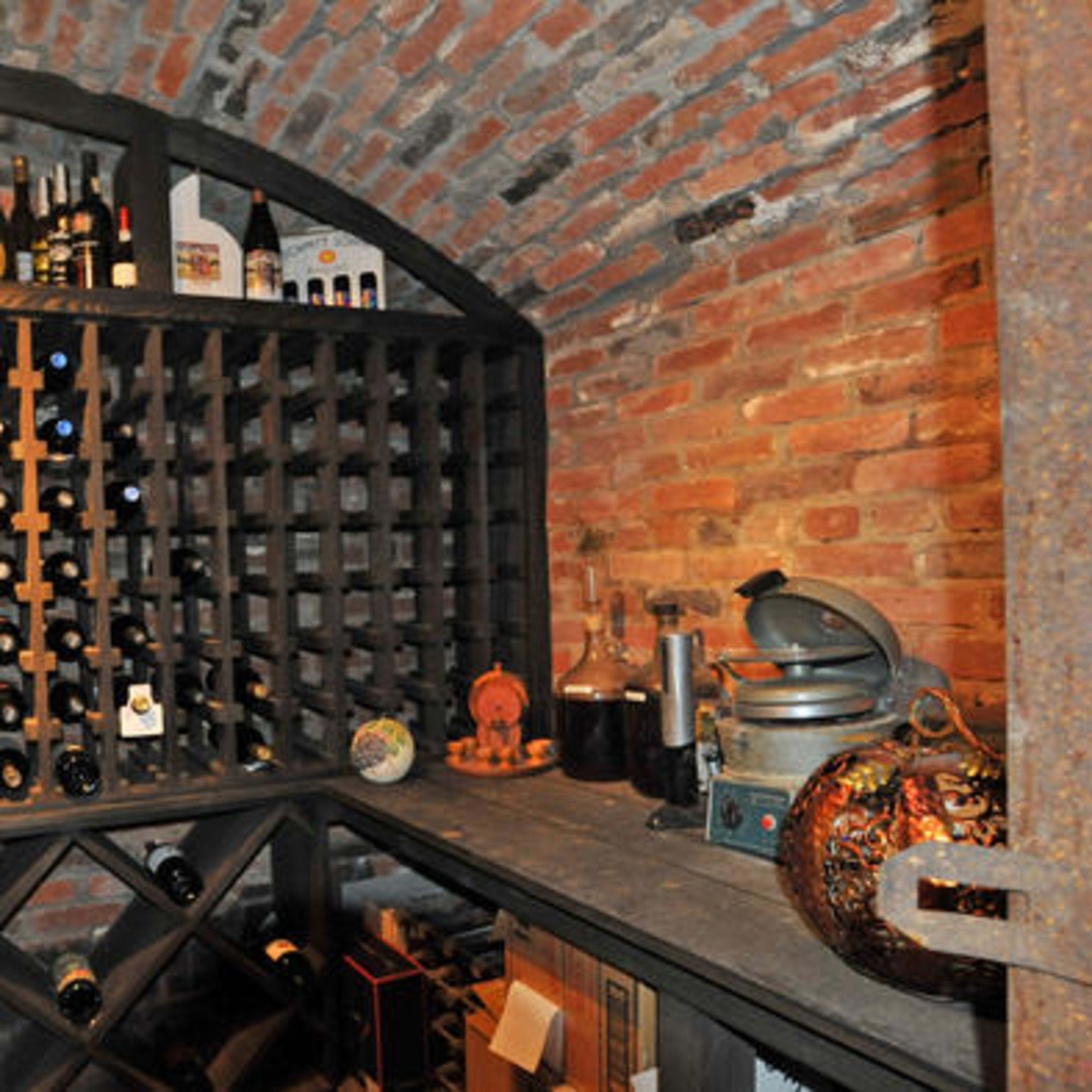 A brick wine cellar with a wooden wine rack filled with bottles and a small table with wine accessories.