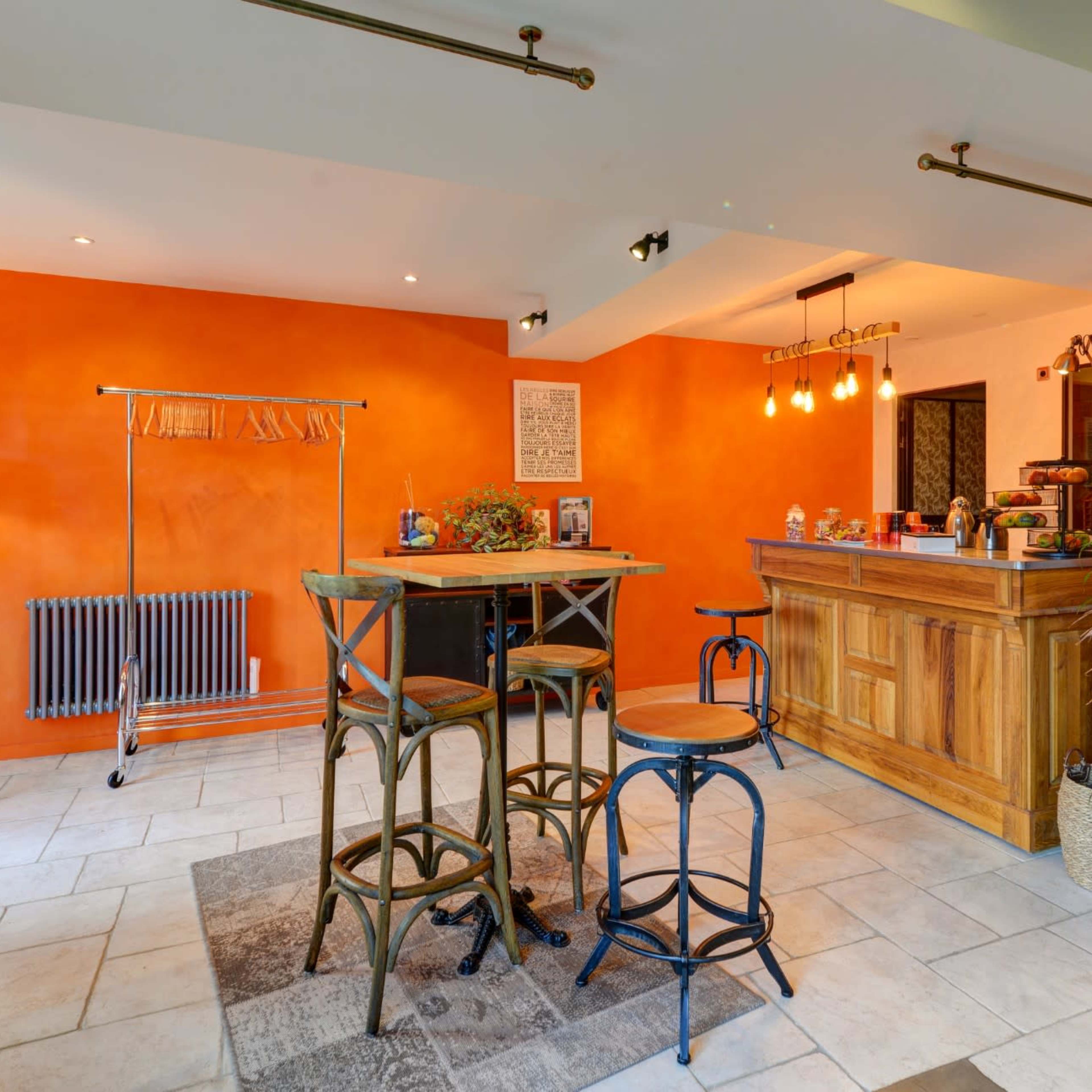A cozy interior of a café with an orange accent wall, wooden bar, and tall stools arranged around a table.