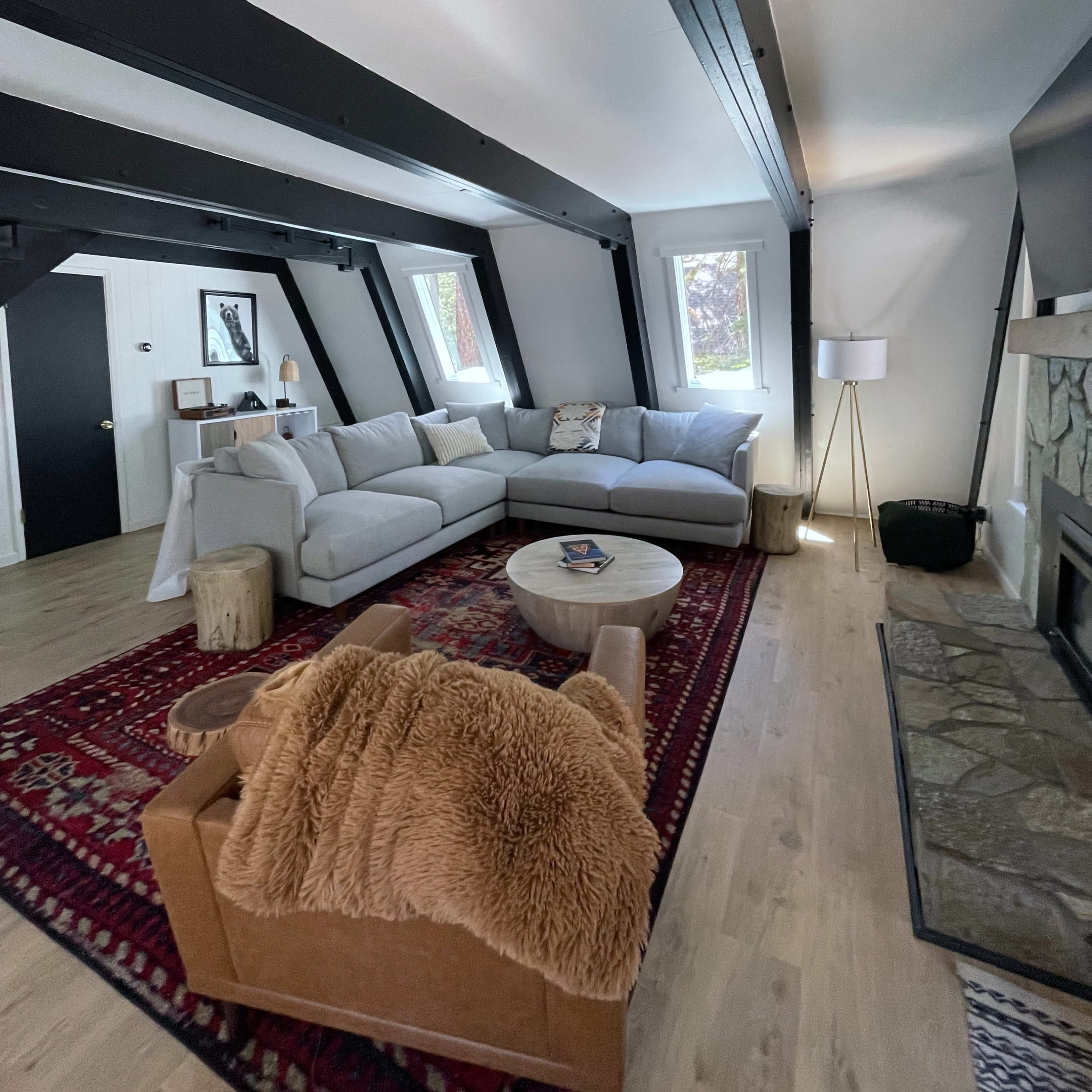 A bright living room with angled ceilings, featuring a large gray sectional sofa, a round coffee table, and a stone fireplace.