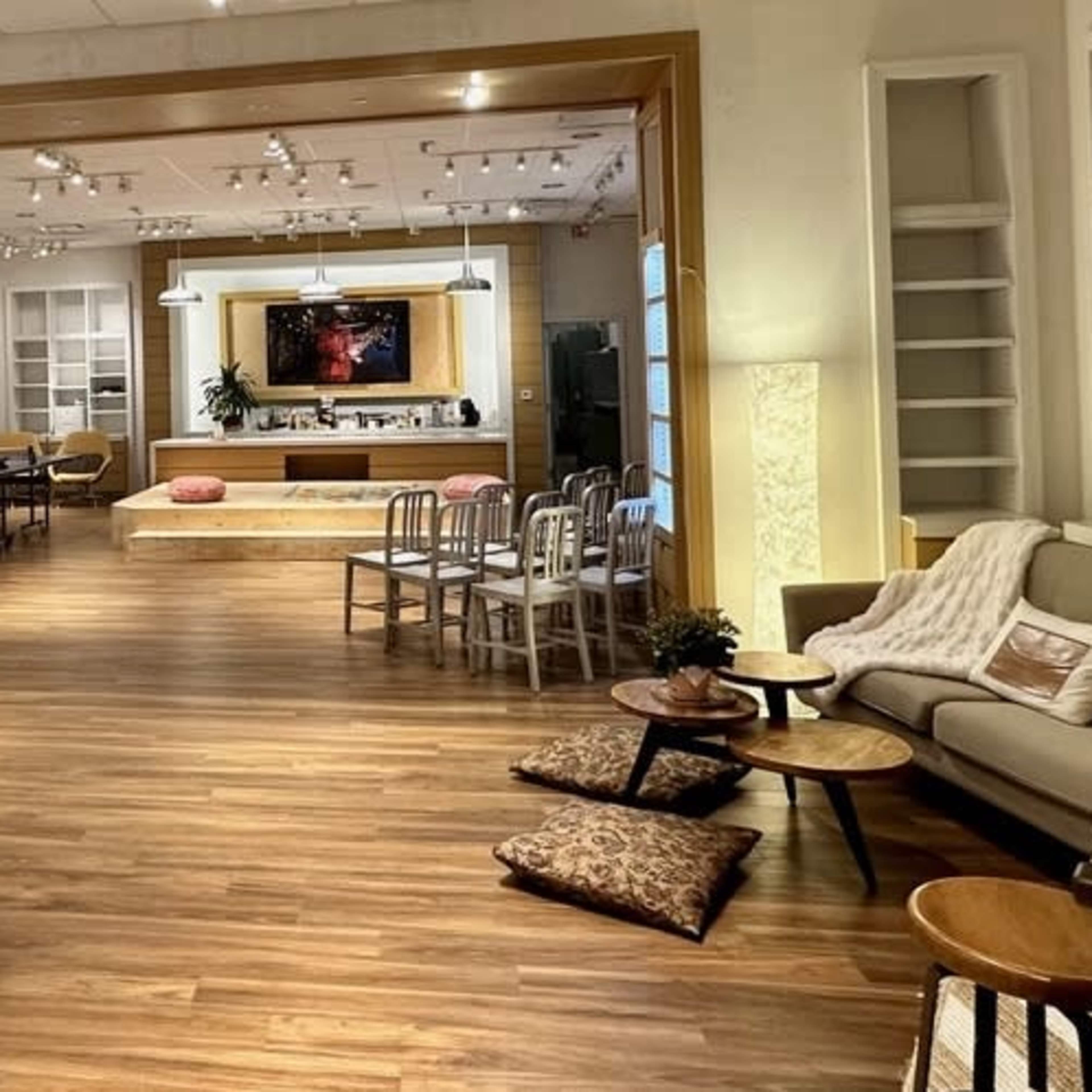 A well-lit interior space featuring a living area with sofas and armchairs, a dining area with tables and chairs, and a versatile layout with wooden flooring.
