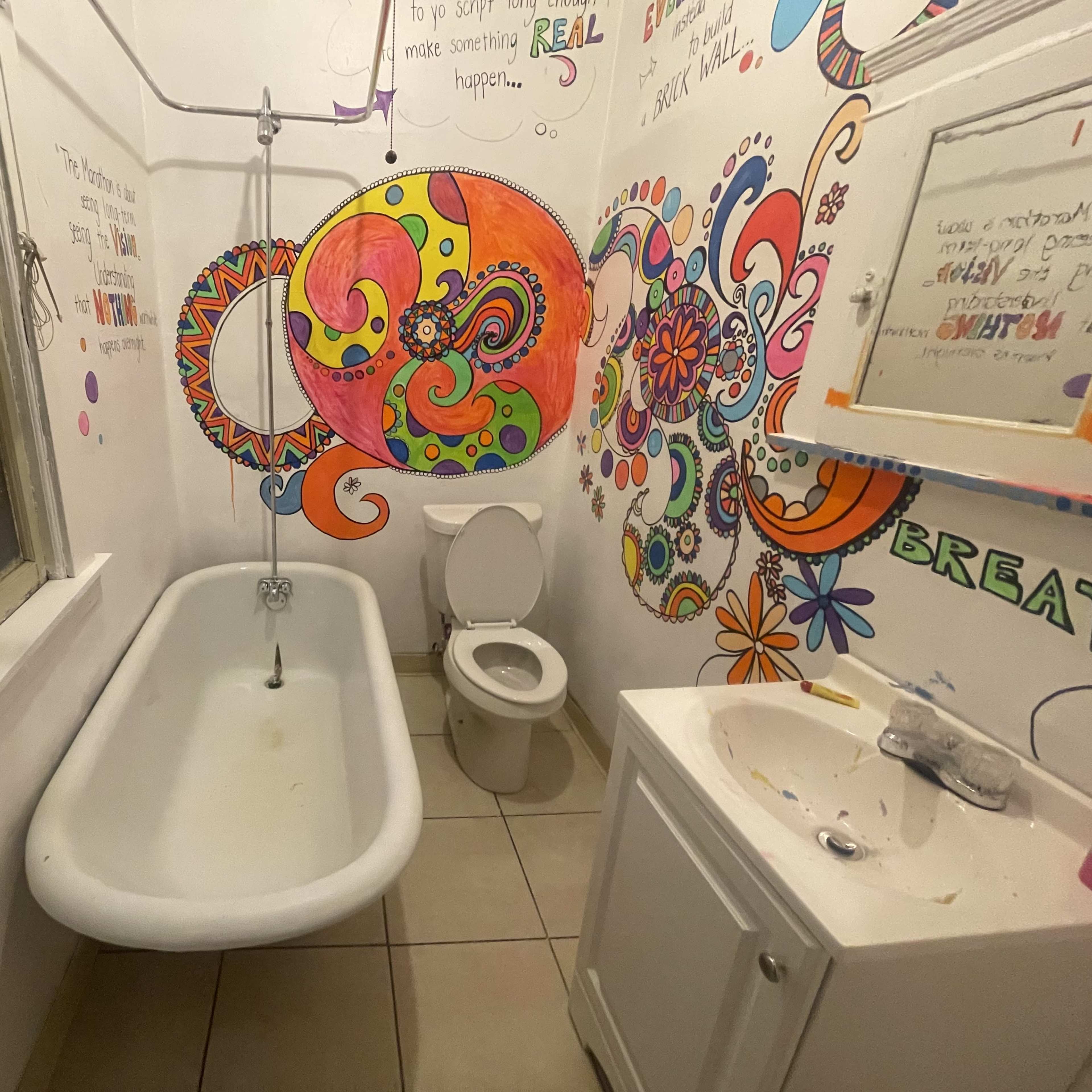 The bathroom features a vintage clawfoot bathtub, a toilet, and a sink surrounded by colorful, whimsical wall art.