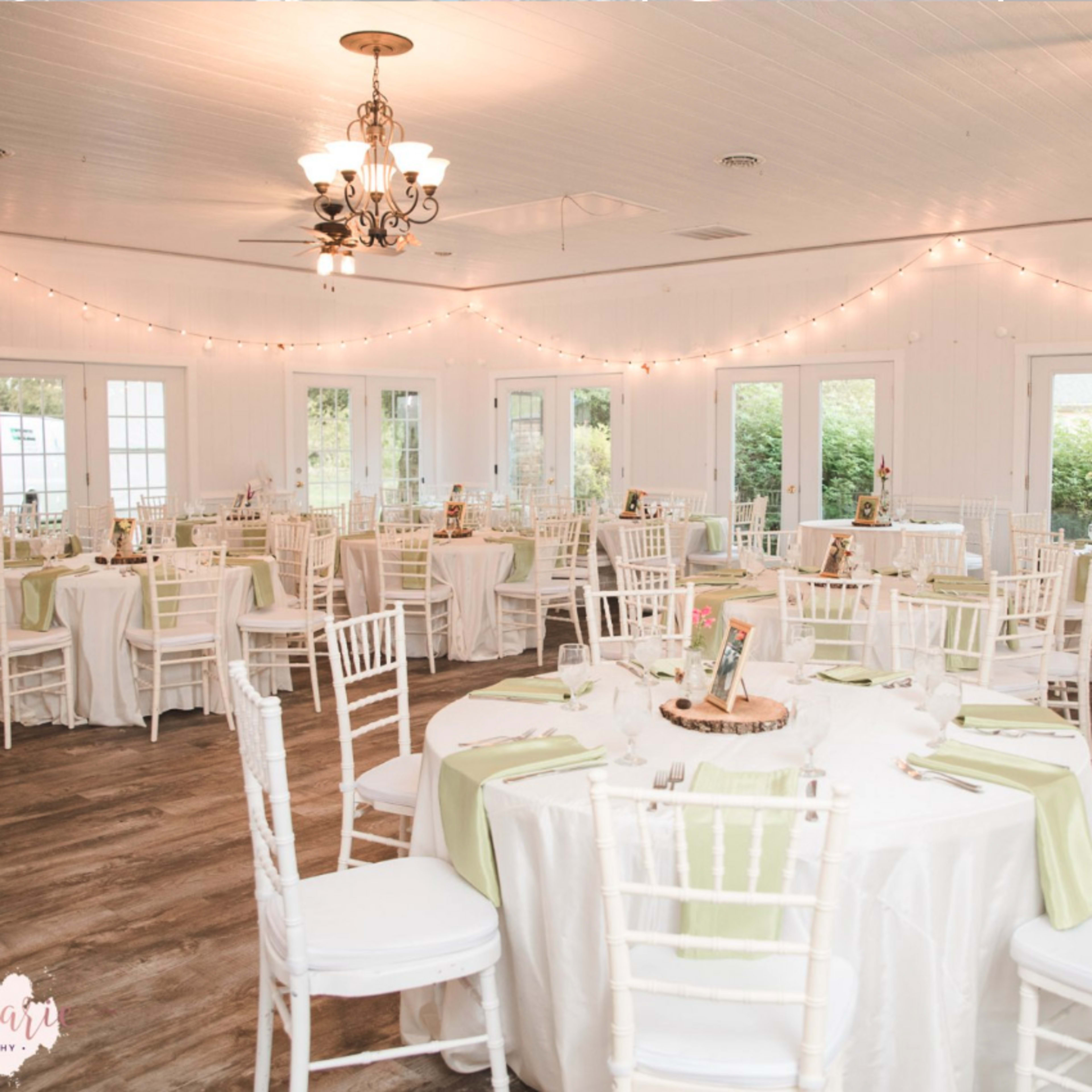 A well-decorated event space featuring round tables with white tablecloths and green accents, surrounded by white chairs and illuminated by soft lighting.