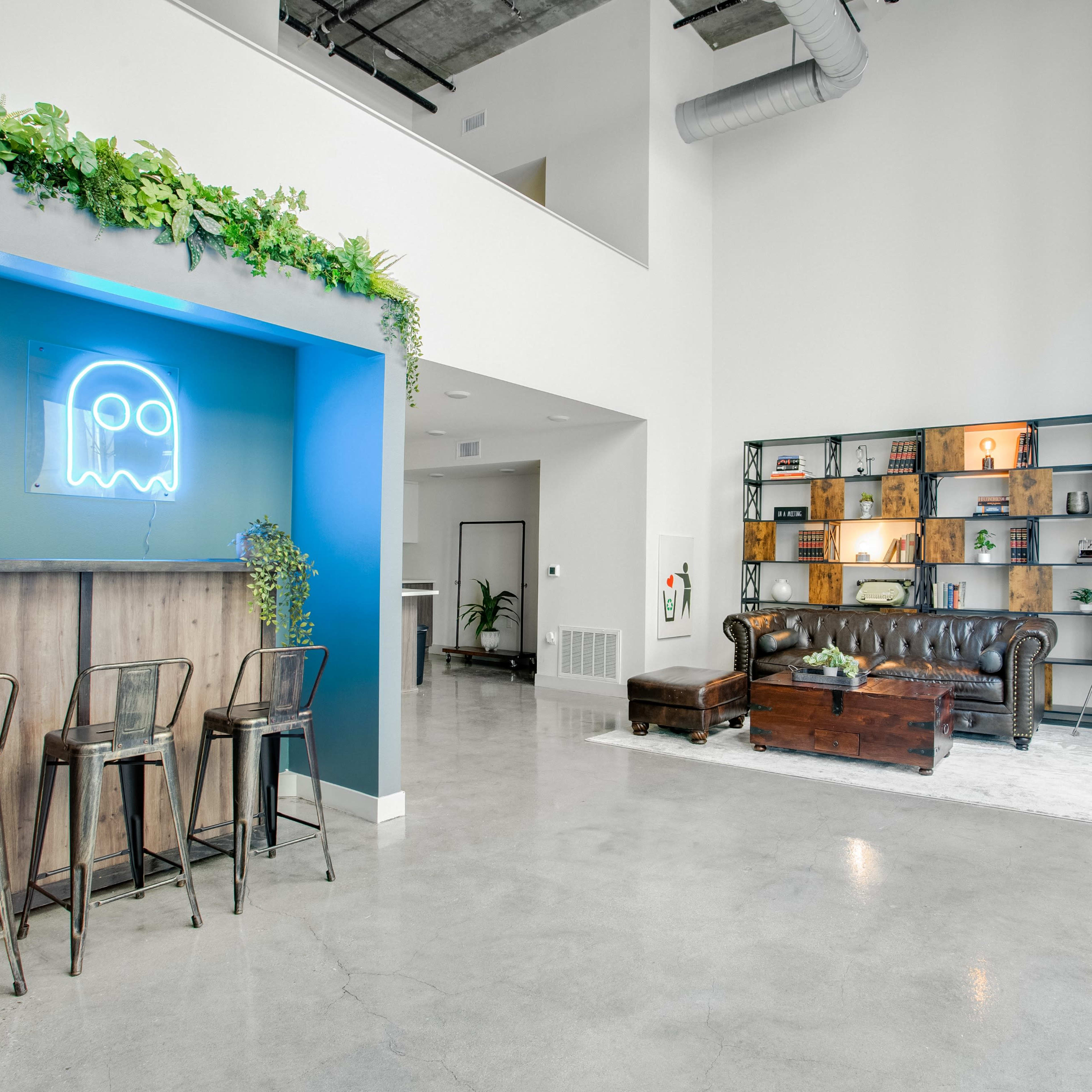 A modern lobby area featuring a bar with high stools on one side and a lounge area with a leather couch and shelves displaying various decorative items on the other.