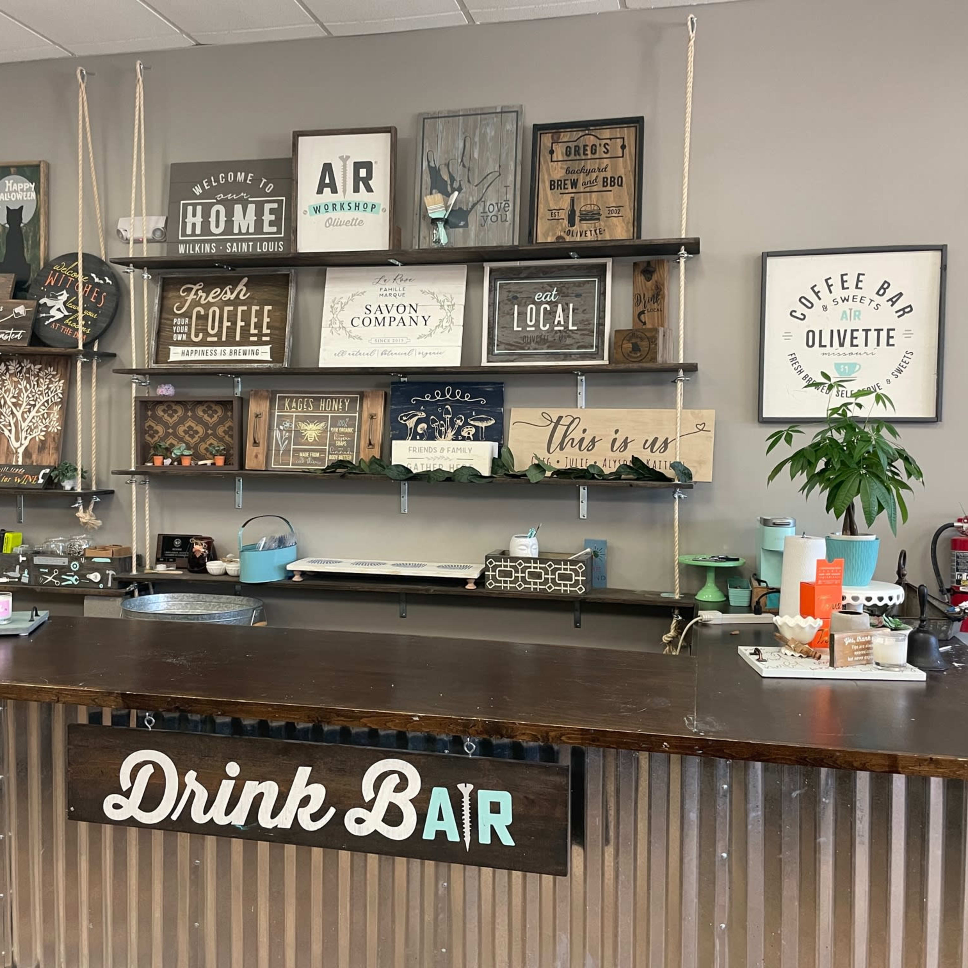 A rustic drink bar featuring various decorative signs and shelves filled with items, set against a neutral wall.
