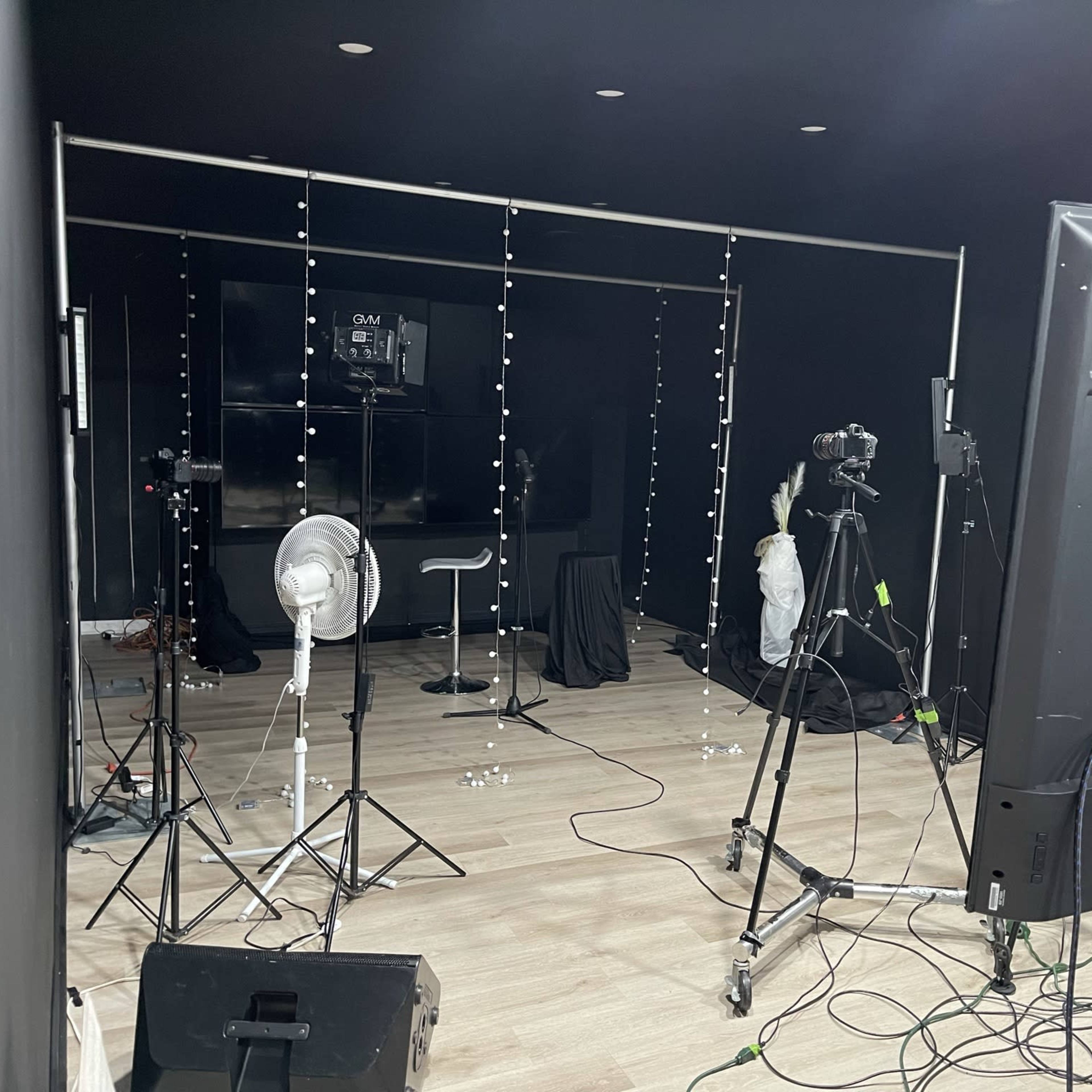 A photography studio setup with cameras, lighting equipment, and a backdrop of black curtains.