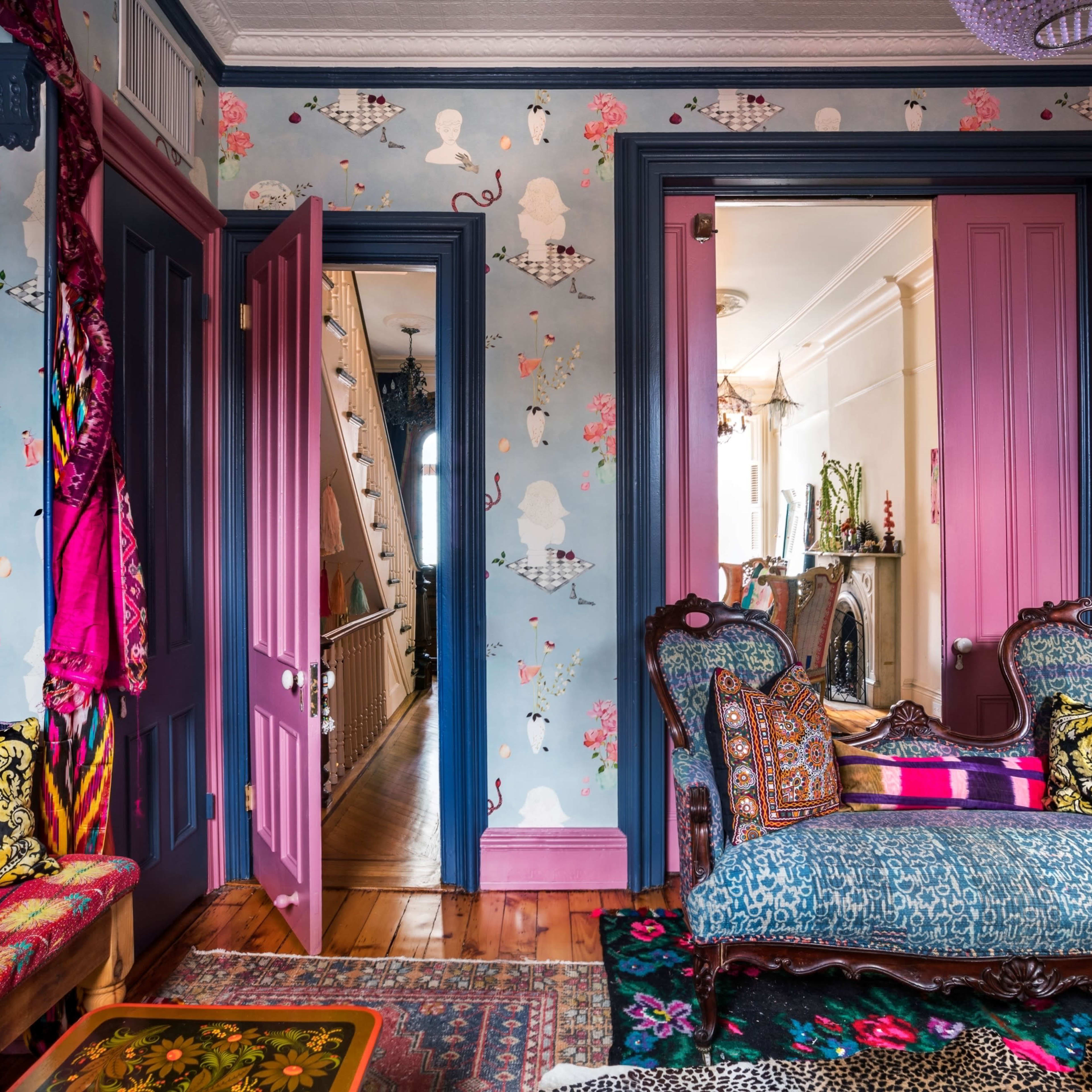 A vibrant room with patterned wallpaper, colorful furniture, and a view into a hallway adorned with decorative elements.