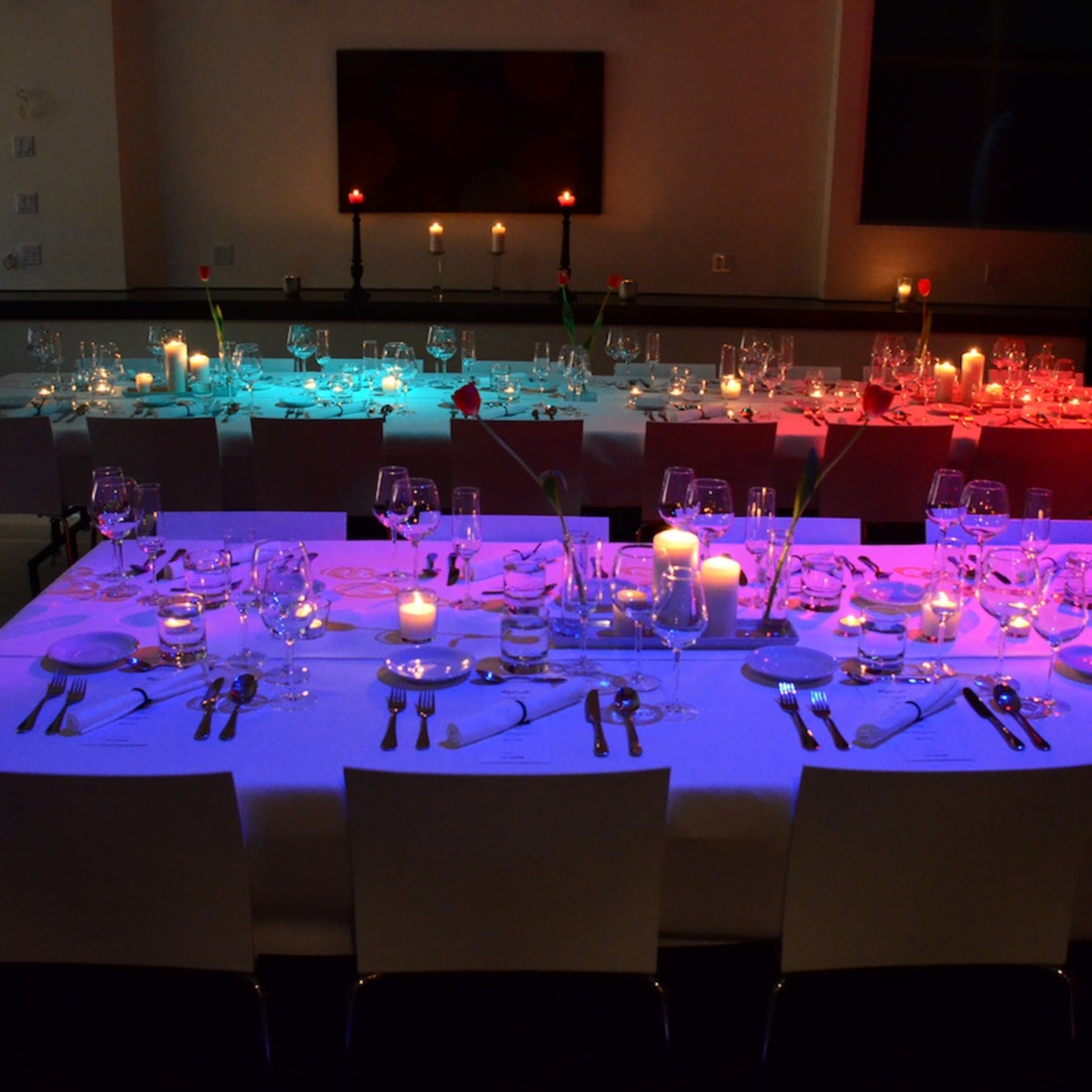 A group of people are seated around a dinner table while a projection of Earth is displayed on the wall behind them.