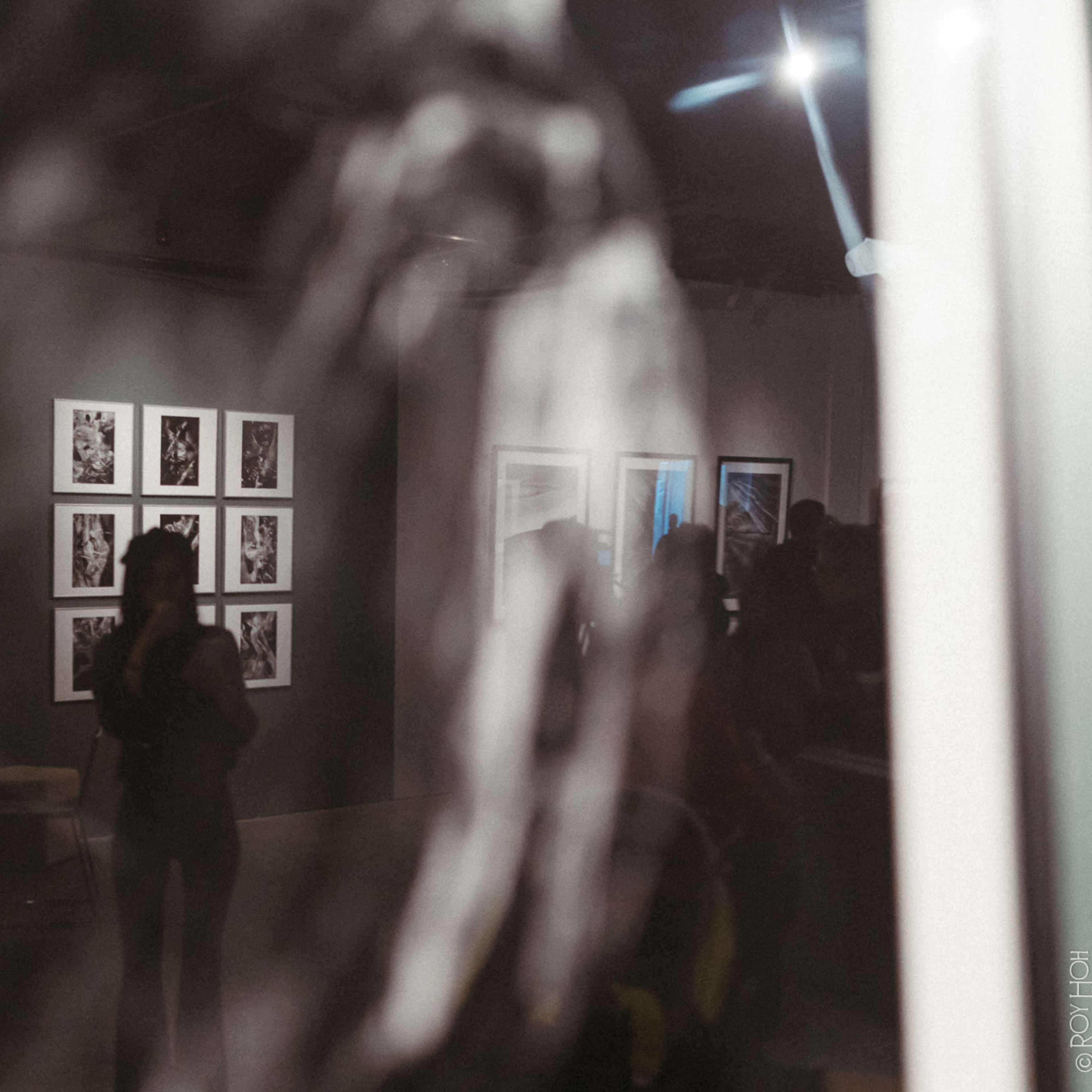 An art gallery with photographs displayed on the walls and visitors reflected in the glass.