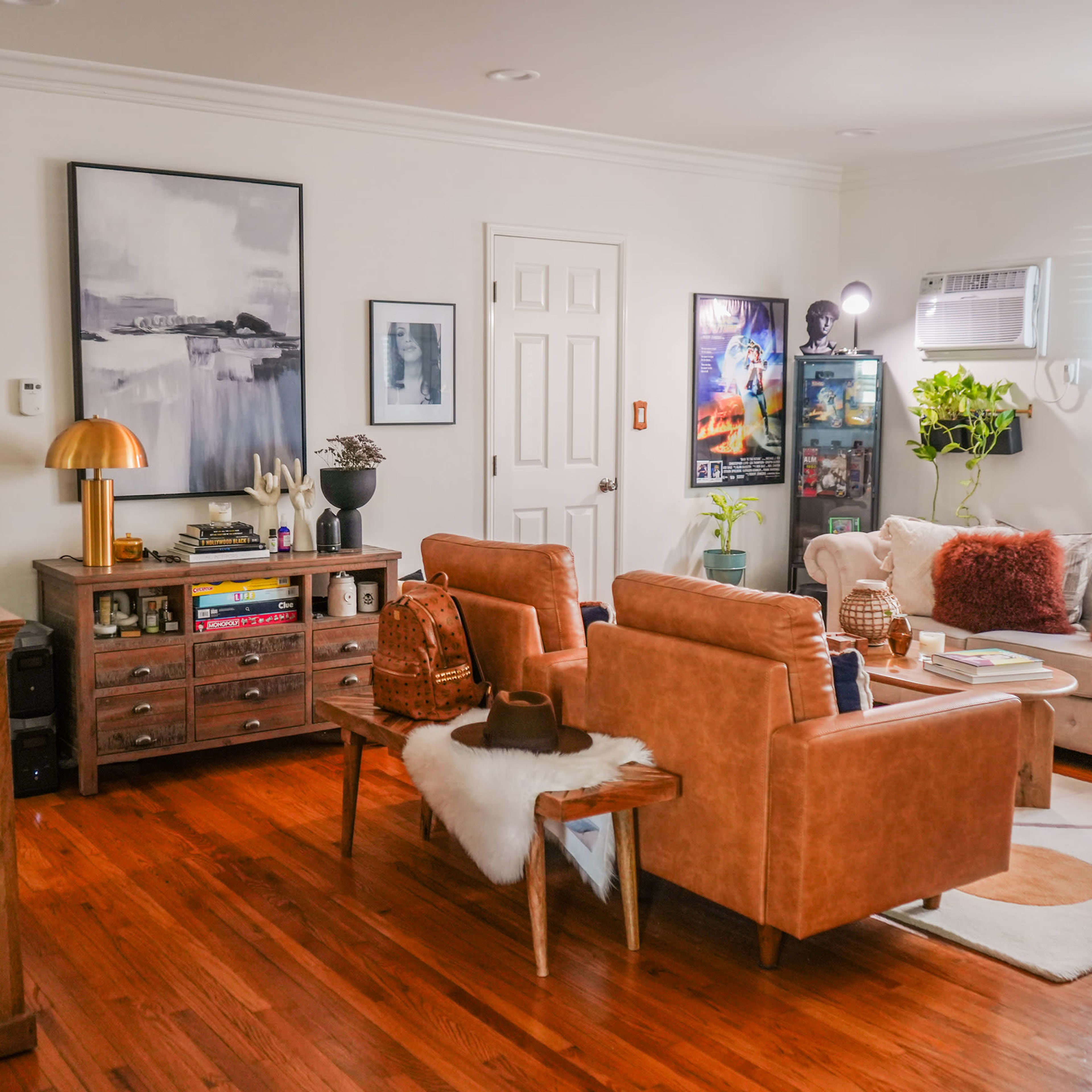A cozy living room with brown leather furniture, a wooden cabinet, and various artworks on the walls.