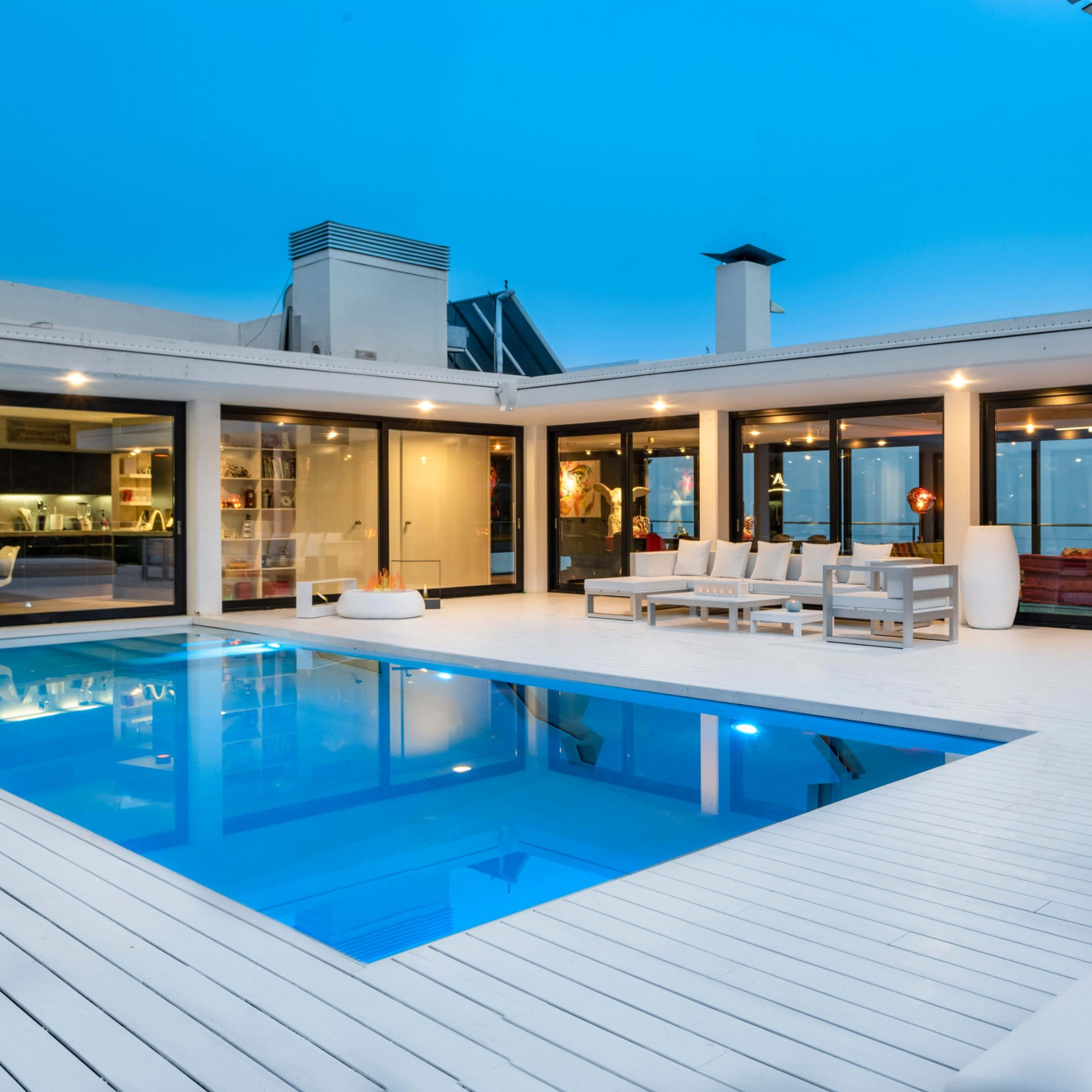 A modern villa with a swimming pool, outdoor seating area, and large glass doors overlooking a scenic view during twilight.