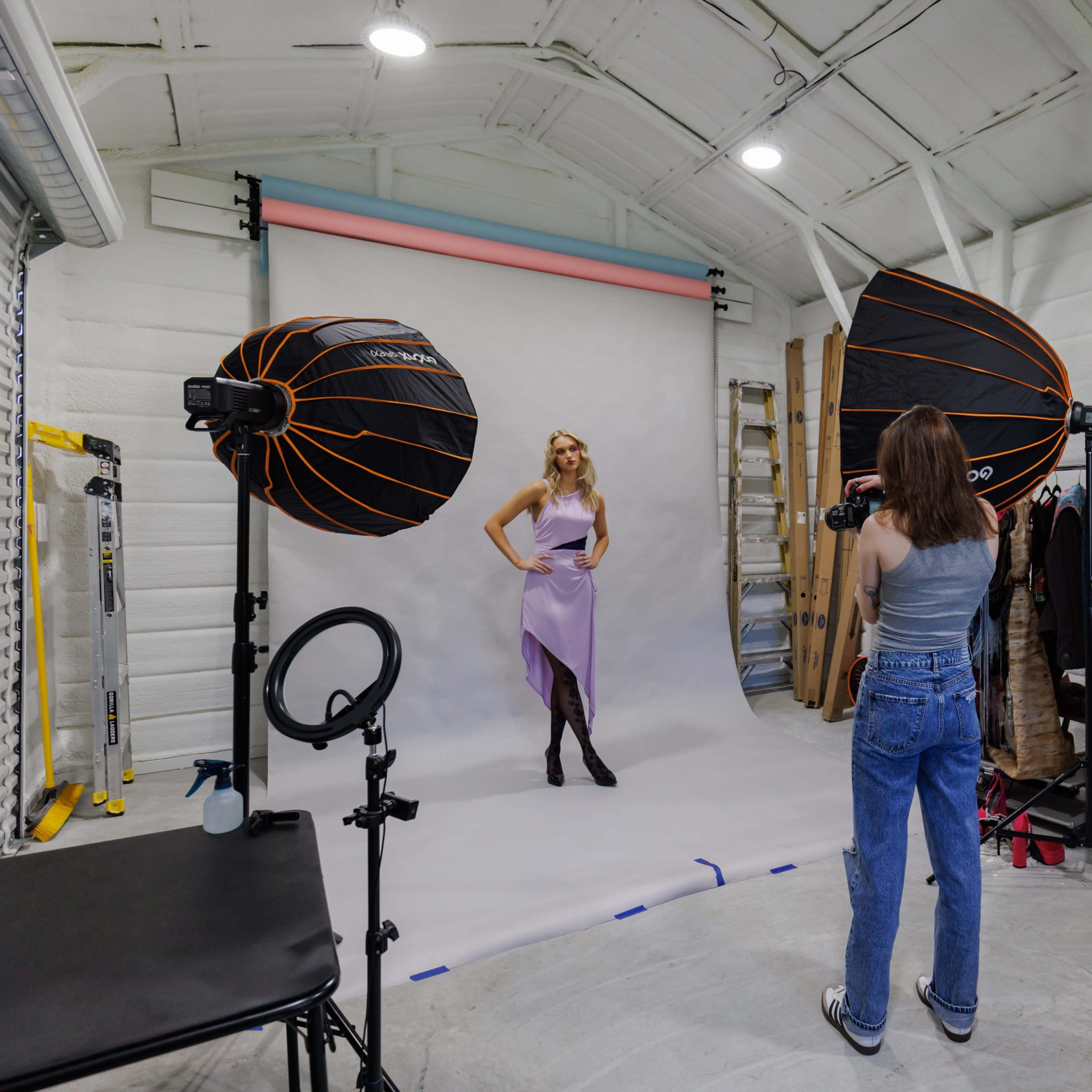 A photographer captures a model posing in front of a backdrop in a studio equipped with softbox lights.