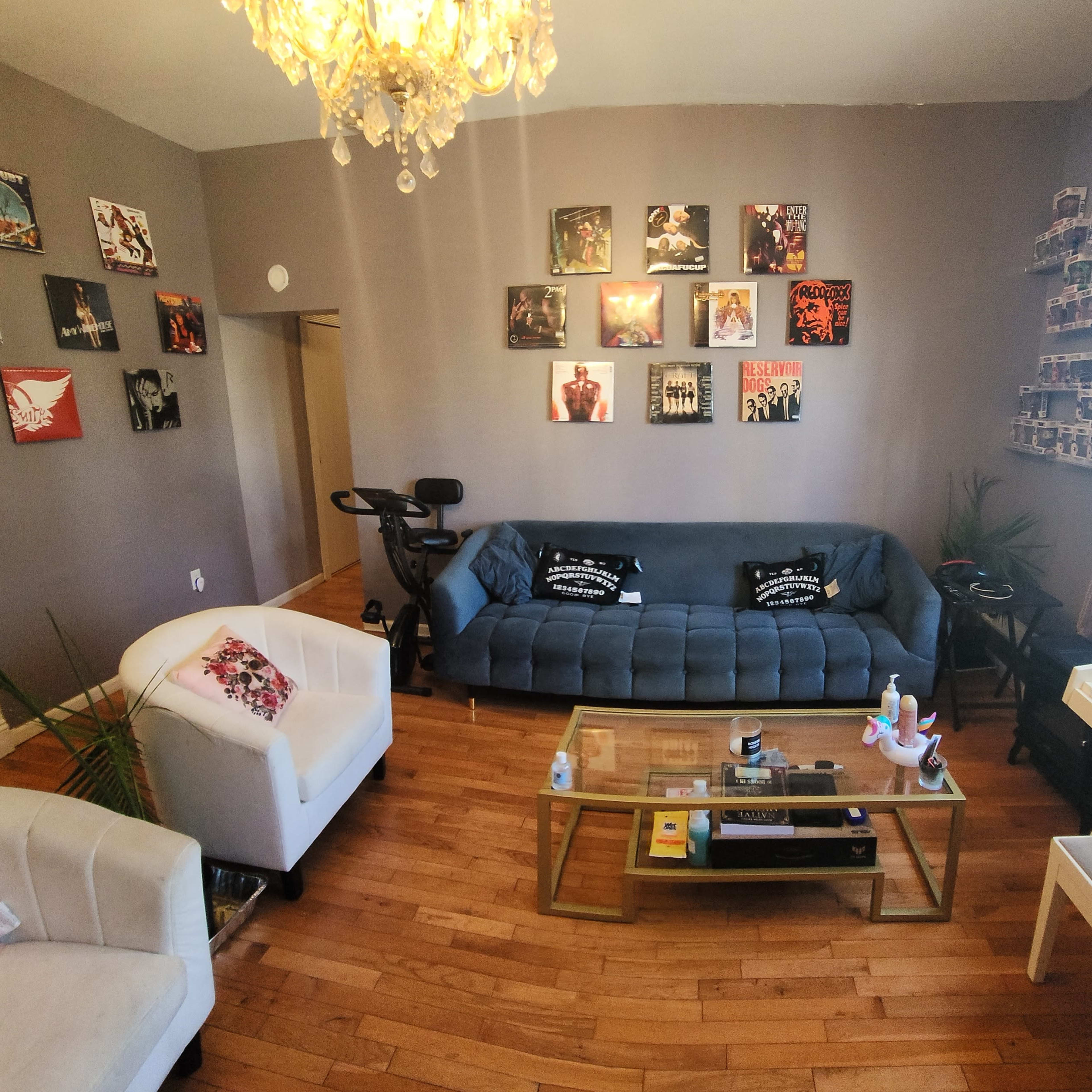 A living room with a blue couch, two white chairs, a coffee table, a piano, and various framed artworks on the walls.