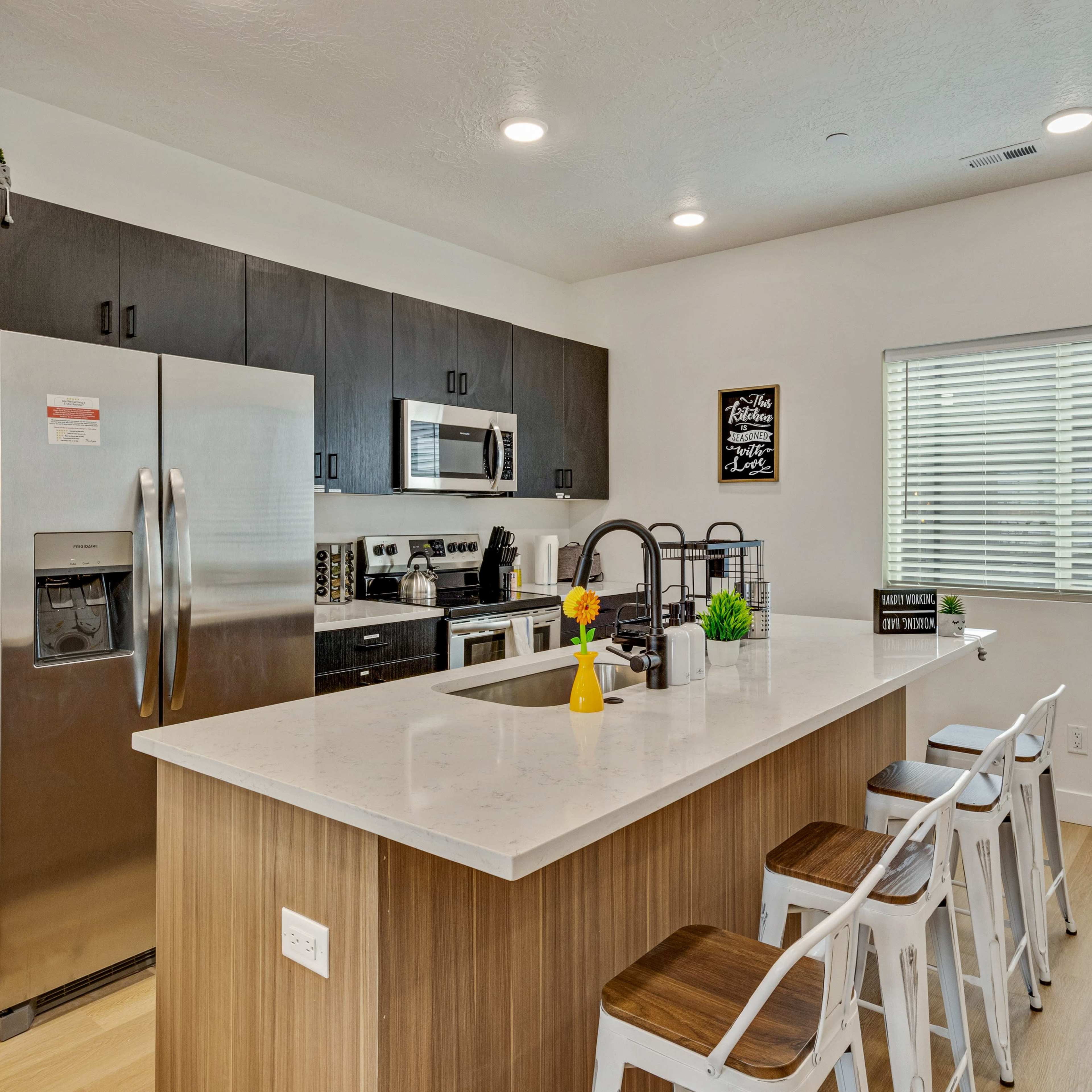A modern kitchen features stainless steel appliances, a large island with bar stools, and sleek cabinetry.