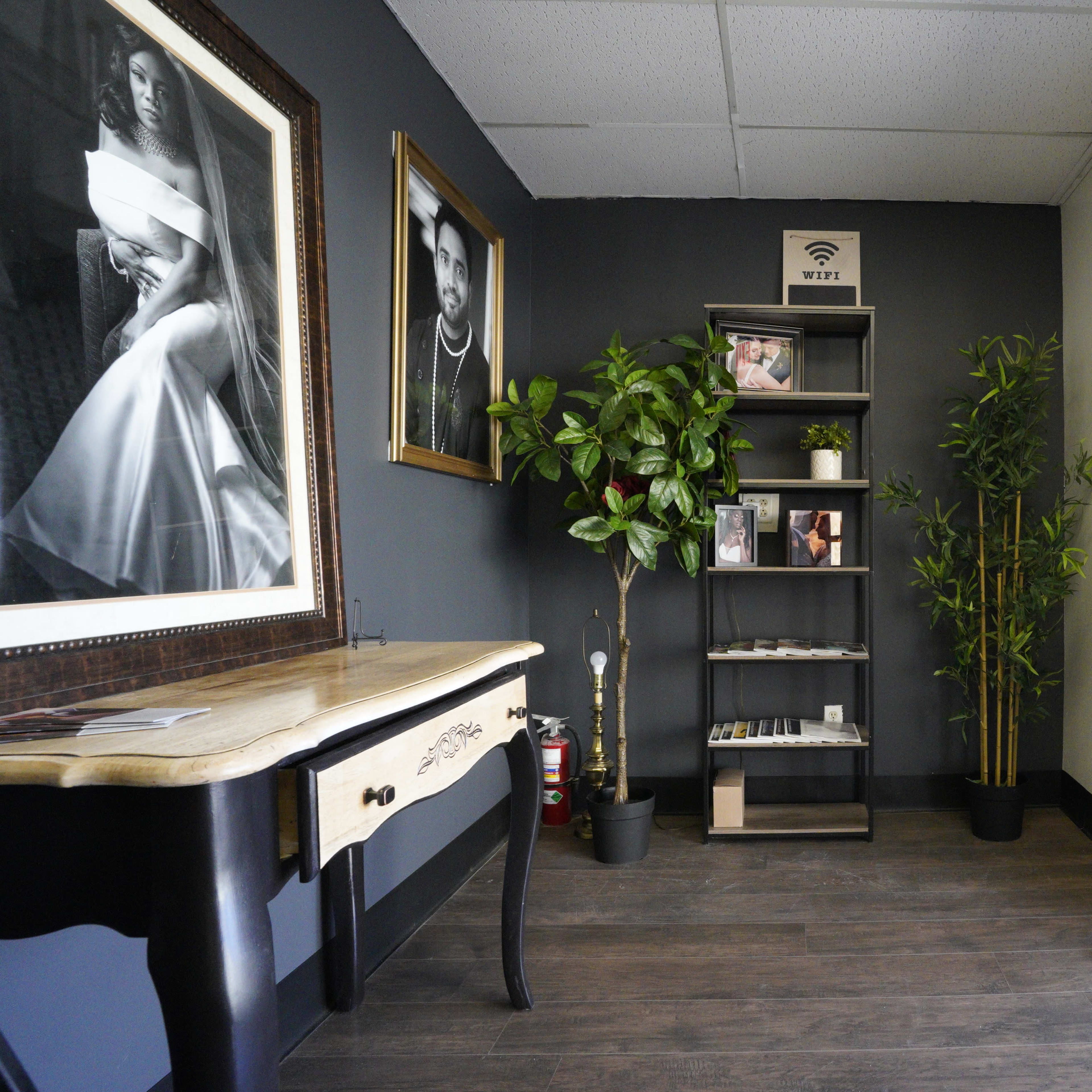 A modern entryway with a wooden table, framed photographs on the wall, a shelf with plants and brochures, and a large glass door leading outside.