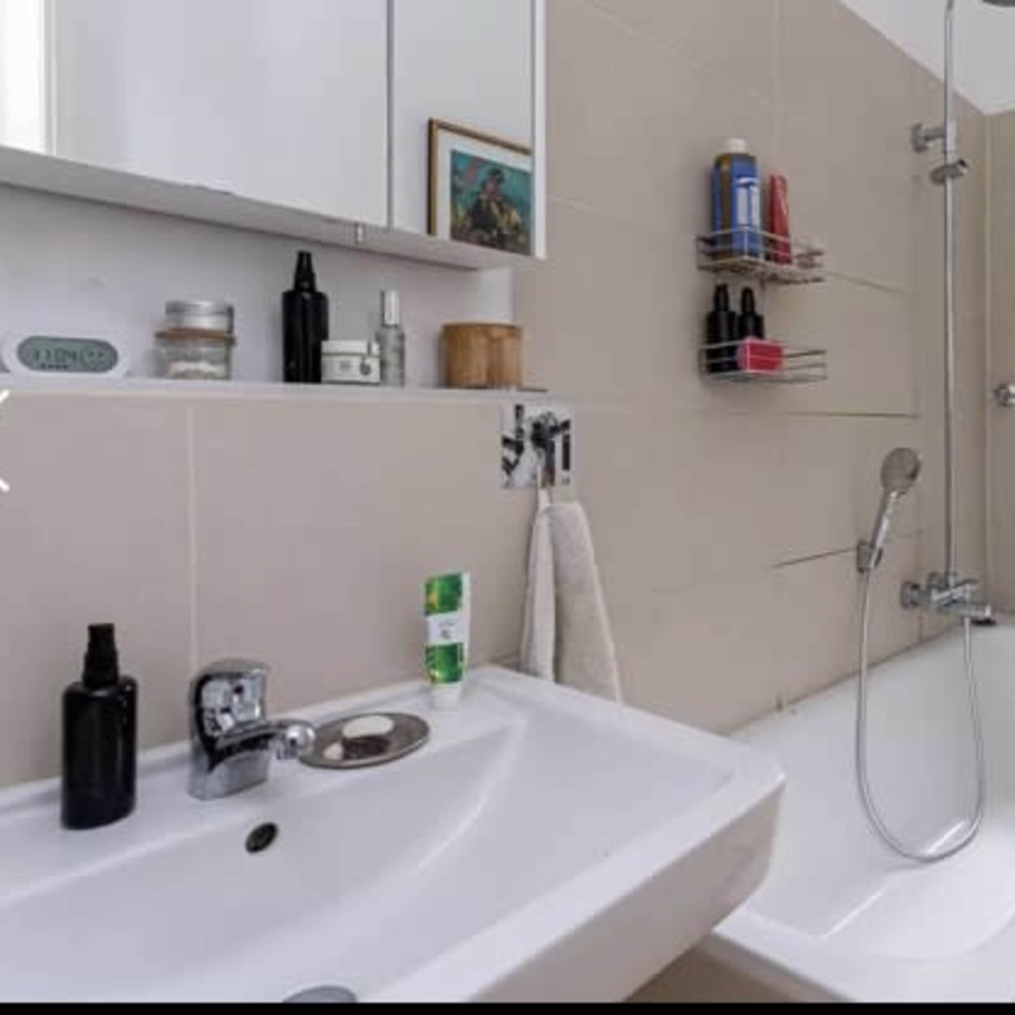A modern bathroom featuring a bathtub with a glass shower enclosure, a sink with toiletries, and a towel rack.