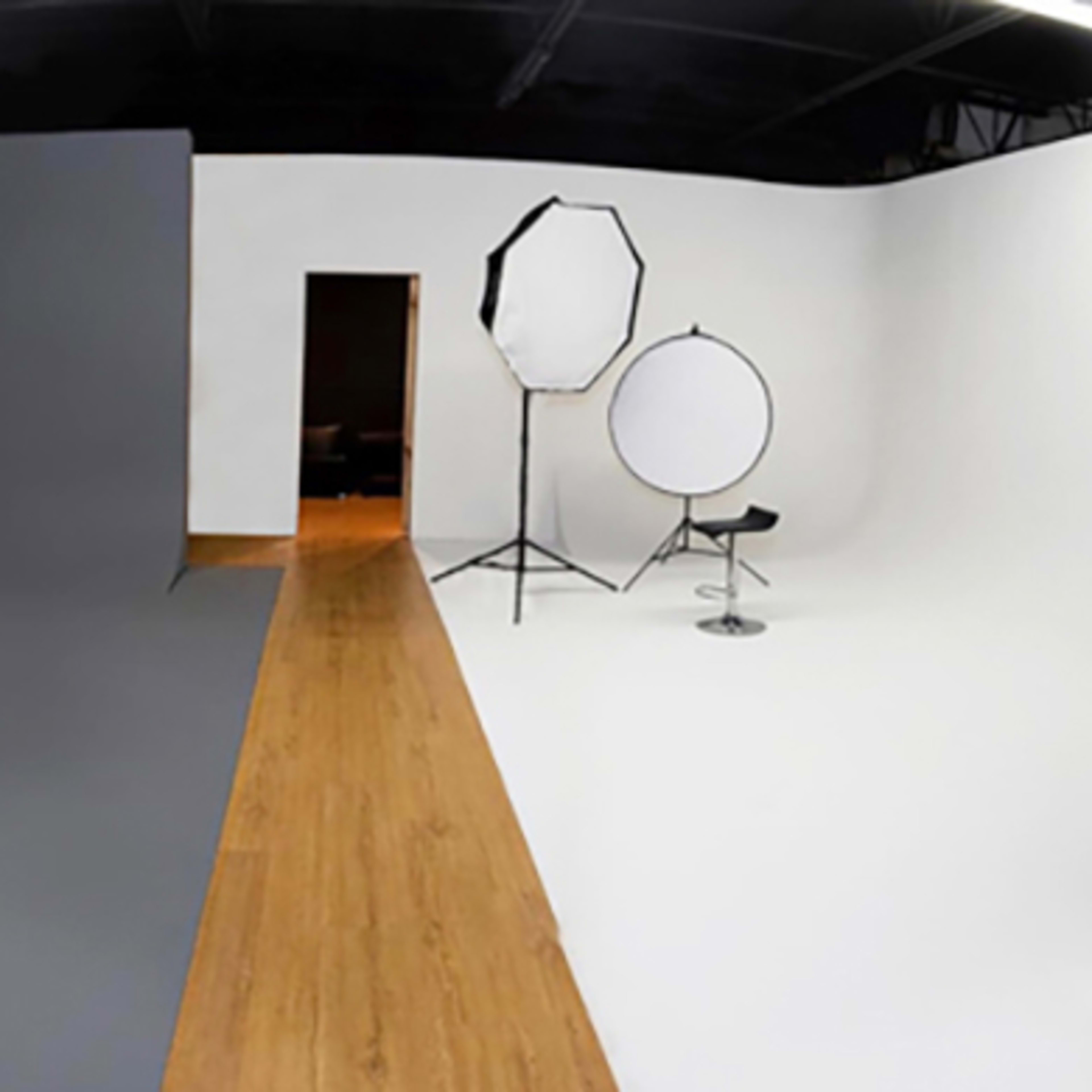 A photography studio features gray and white backdrops with a circular reflector and a stool positioned in the center.