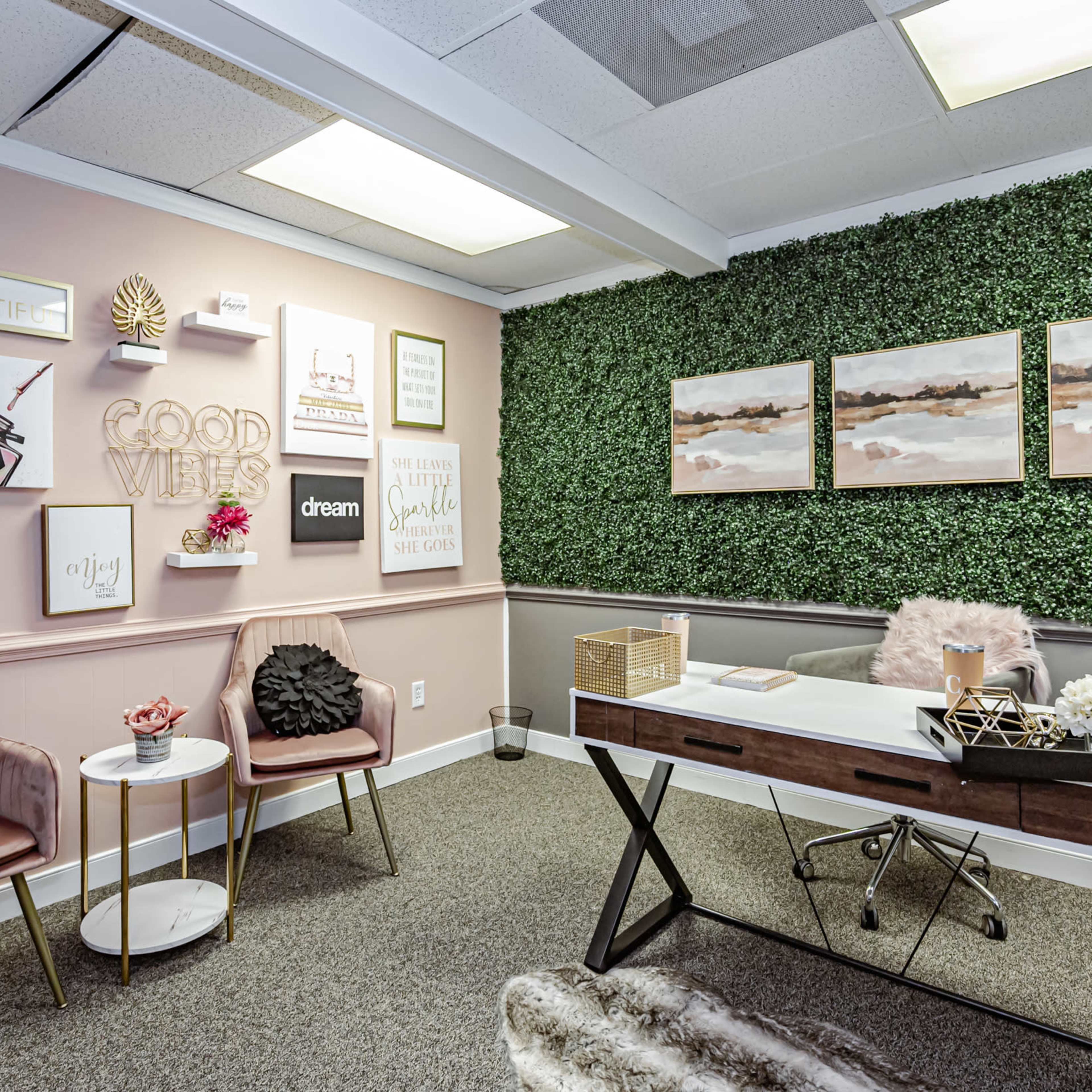 A stylish office space featuring a desk, decorative wall art, two chairs, and a green plant wall.