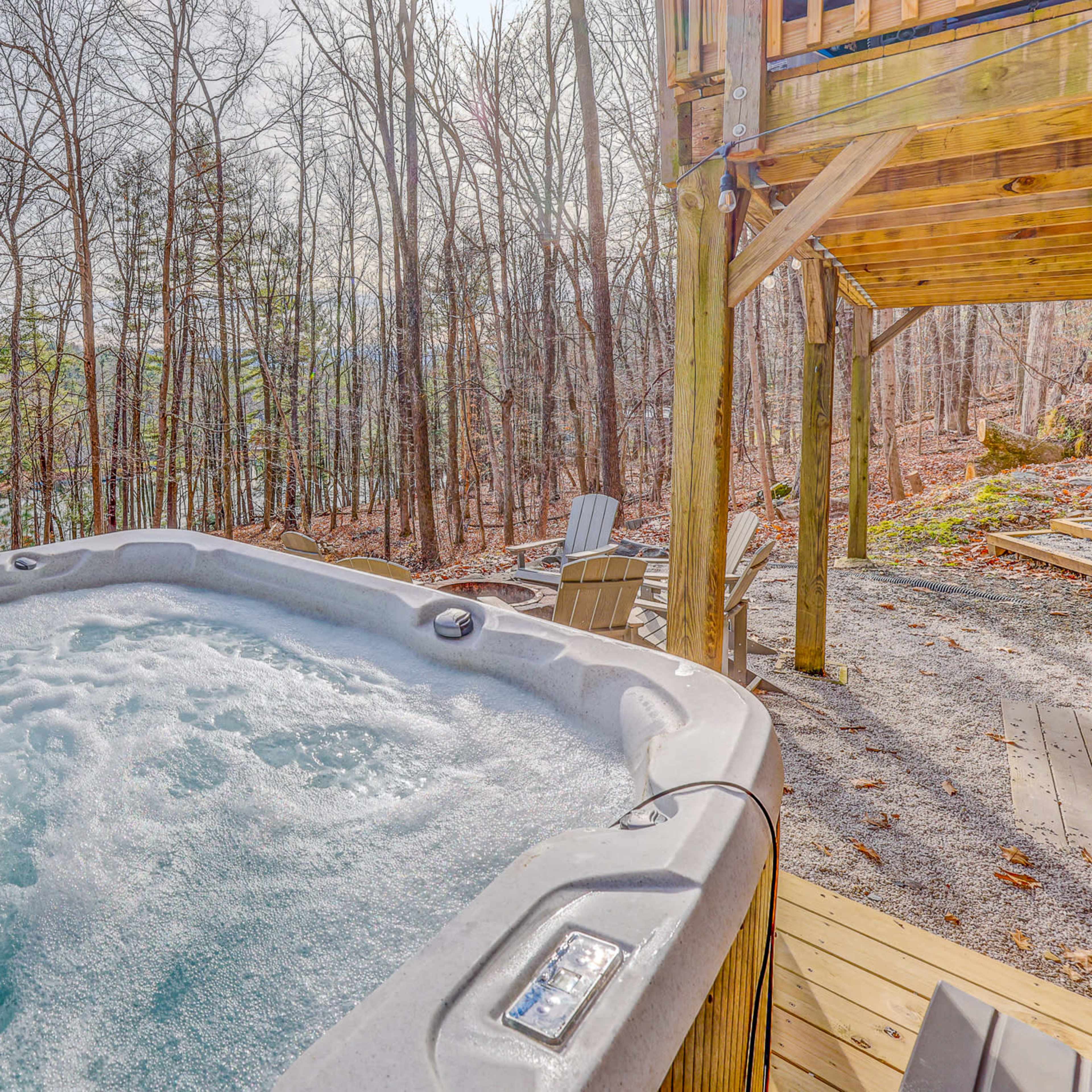 A hot tub filled with bubbles is situated on a wooden deck surrounded by bare trees and a view of a body of water in the background.