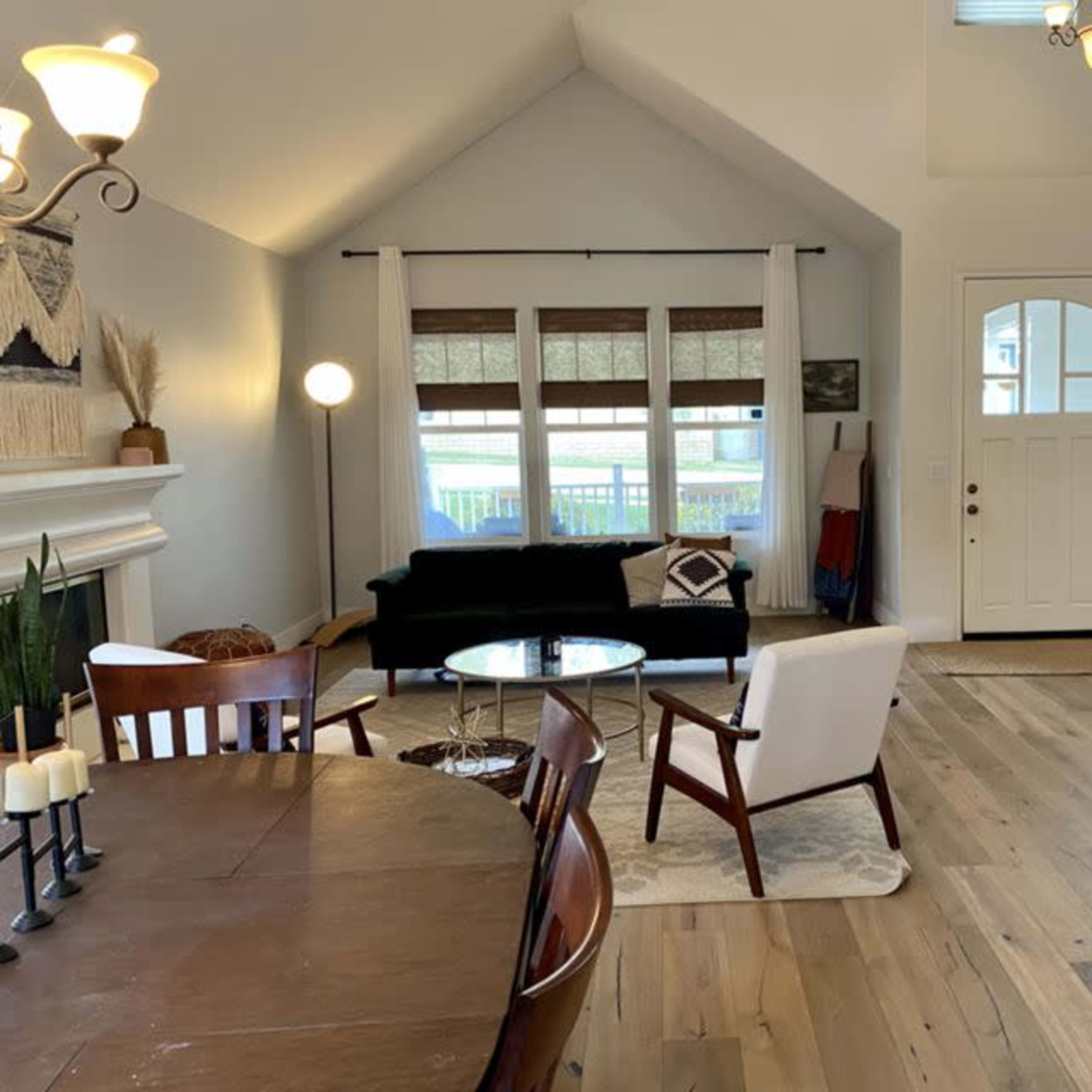 A bright, spacious living room with a mixed seating arrangement, large windows, and an entryway leading to a staircase.
