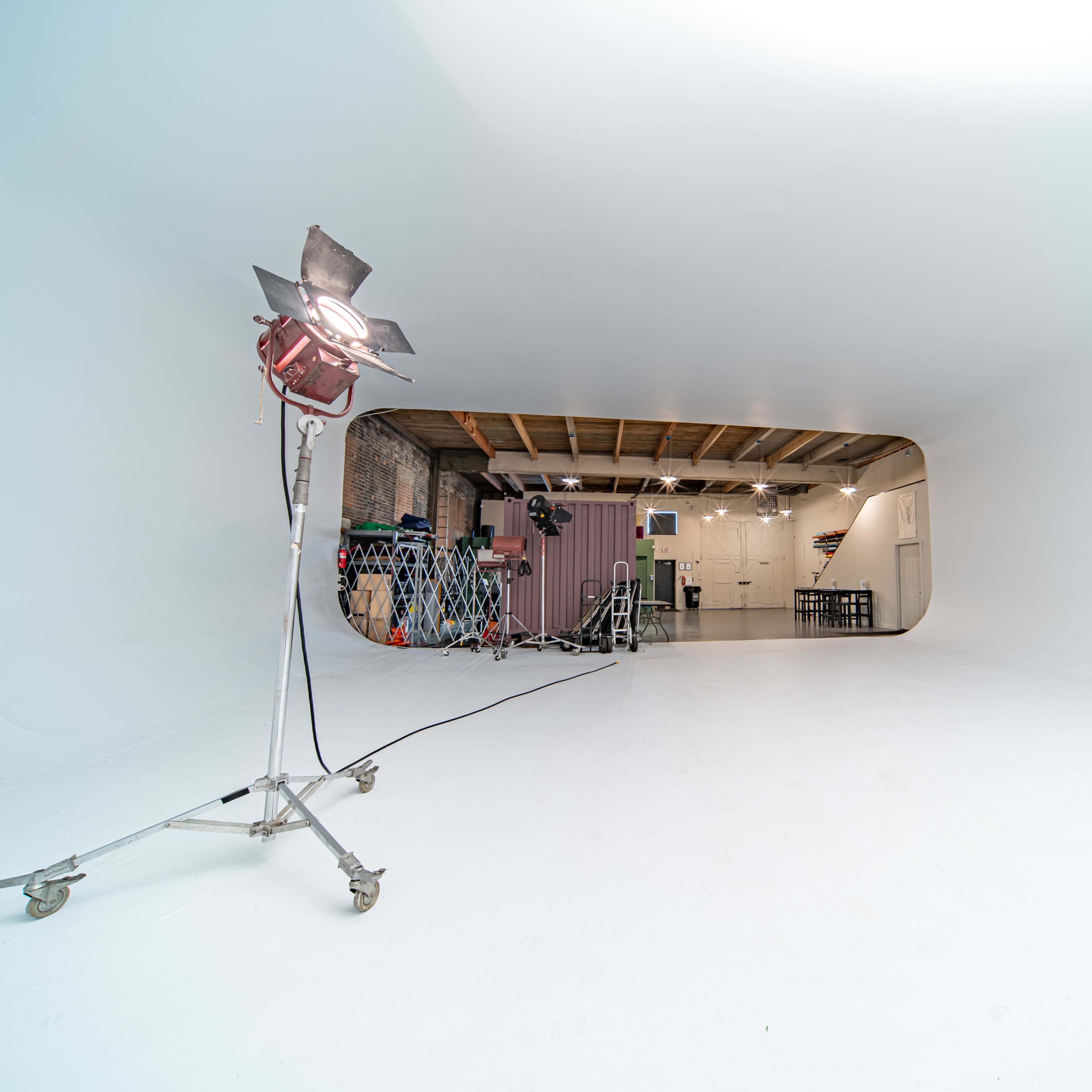 A minimalistic studio space with a bright white backdrop, equipment on wheels, and a lighting fixture positioned on the left.