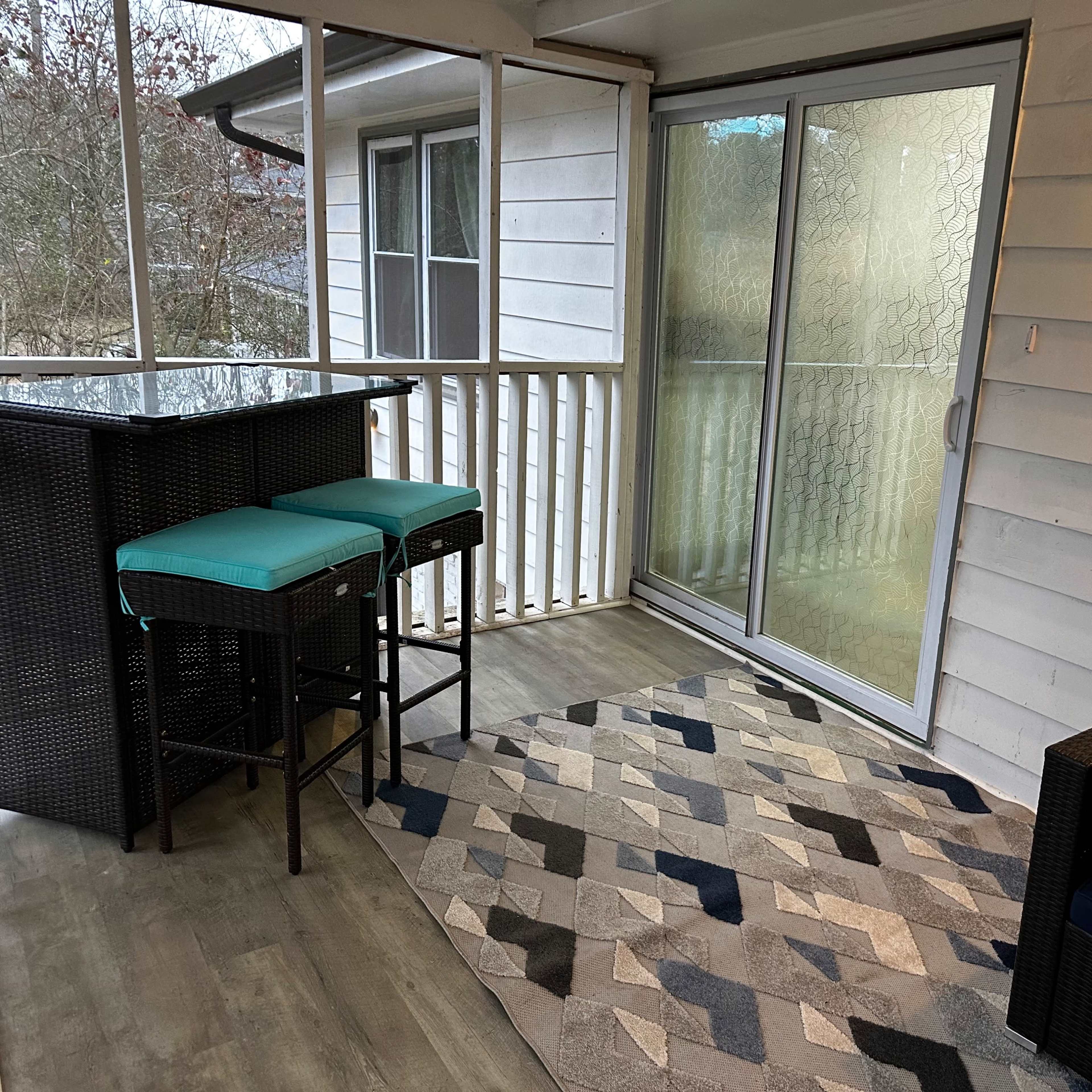 A screened-in porch featuring a bar with two stools, a couch, and a patterned rug.