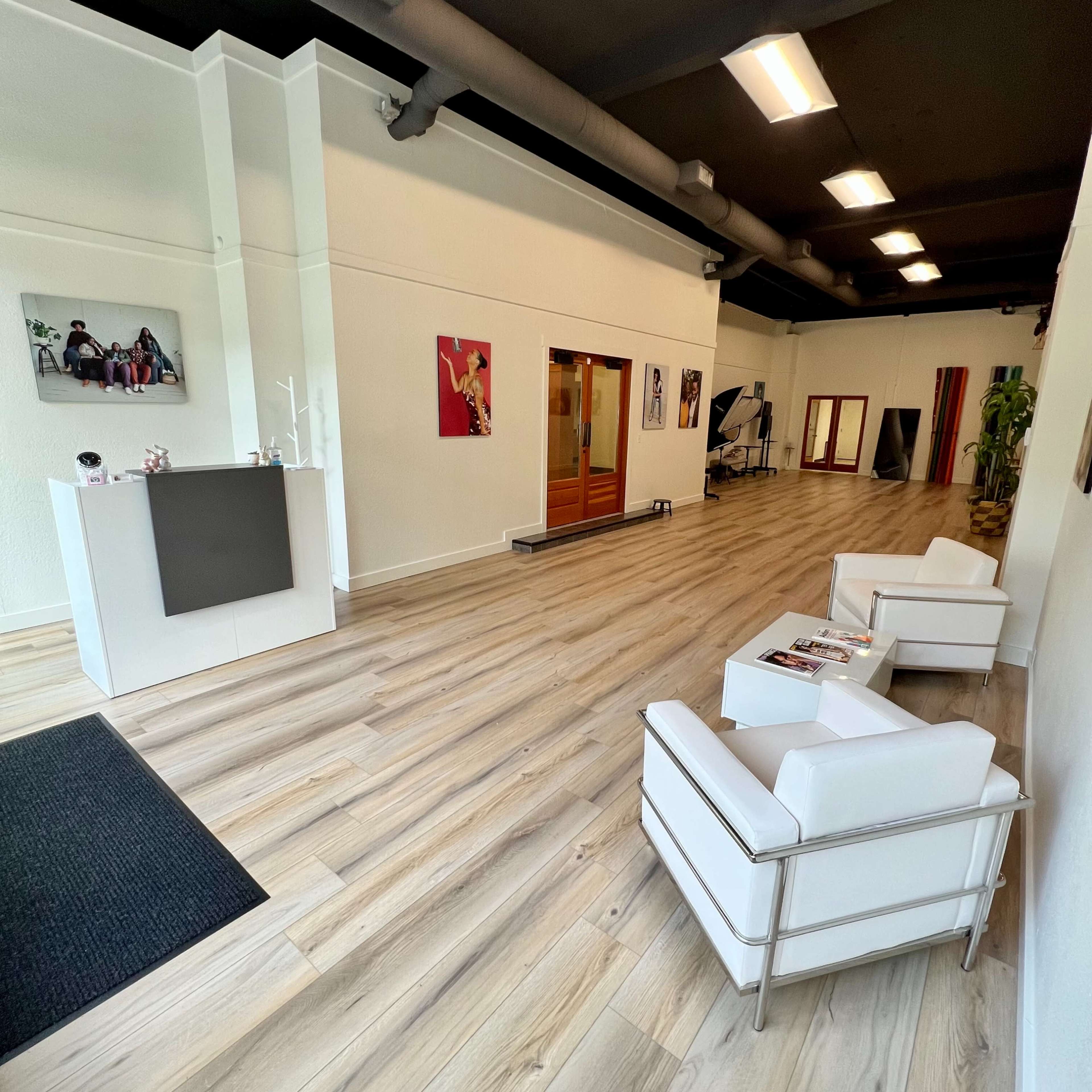 A modern interior of a commercial space with white furnishings, a reception area, and hardwood flooring.