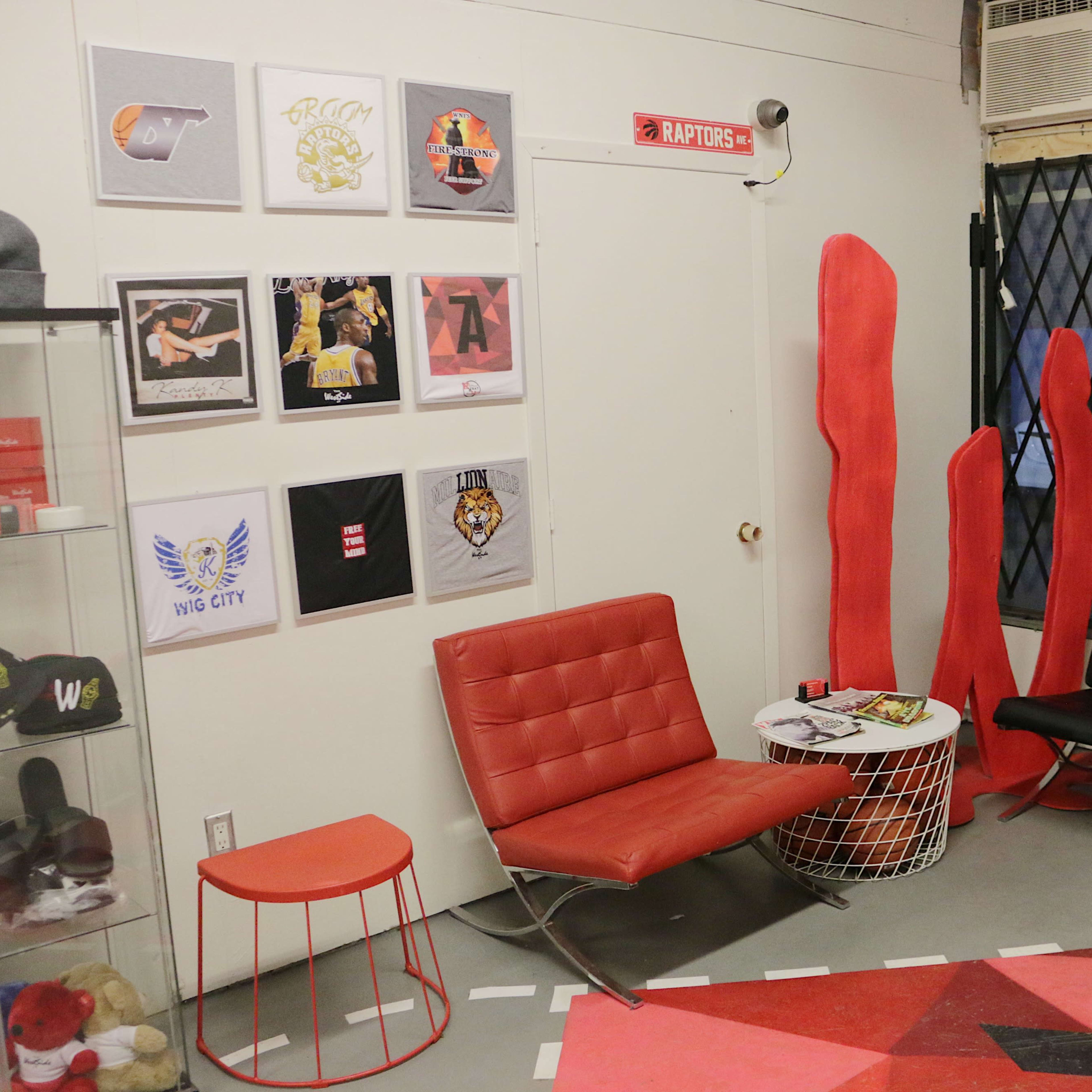 A modern corner of a store featuring black and red seating, a red side table, wall art with various designs, and a security gate in the background.
