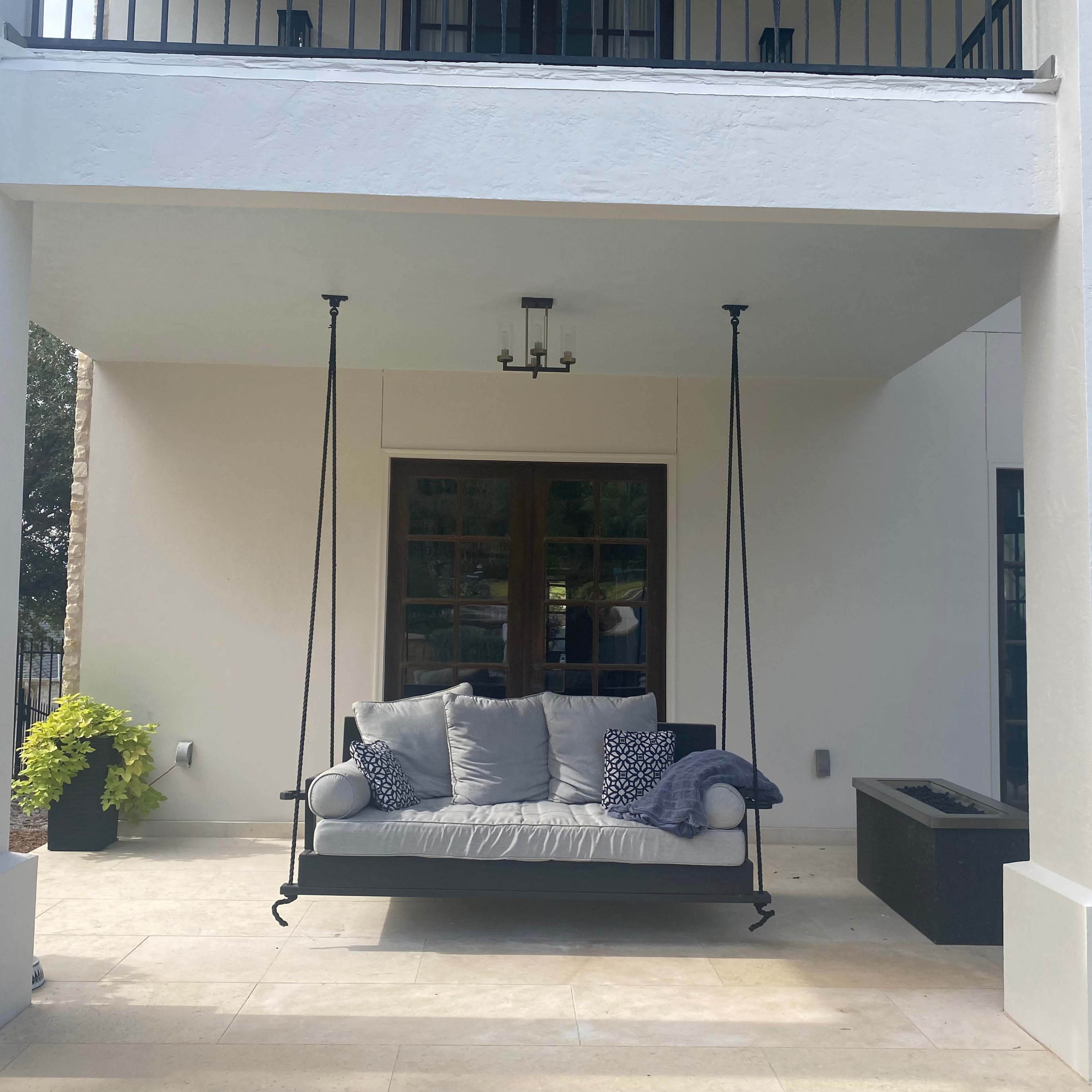 A covered outdoor area featuring a swinging bench with cushions and decorative pillows, along with a fire pit nearby.
