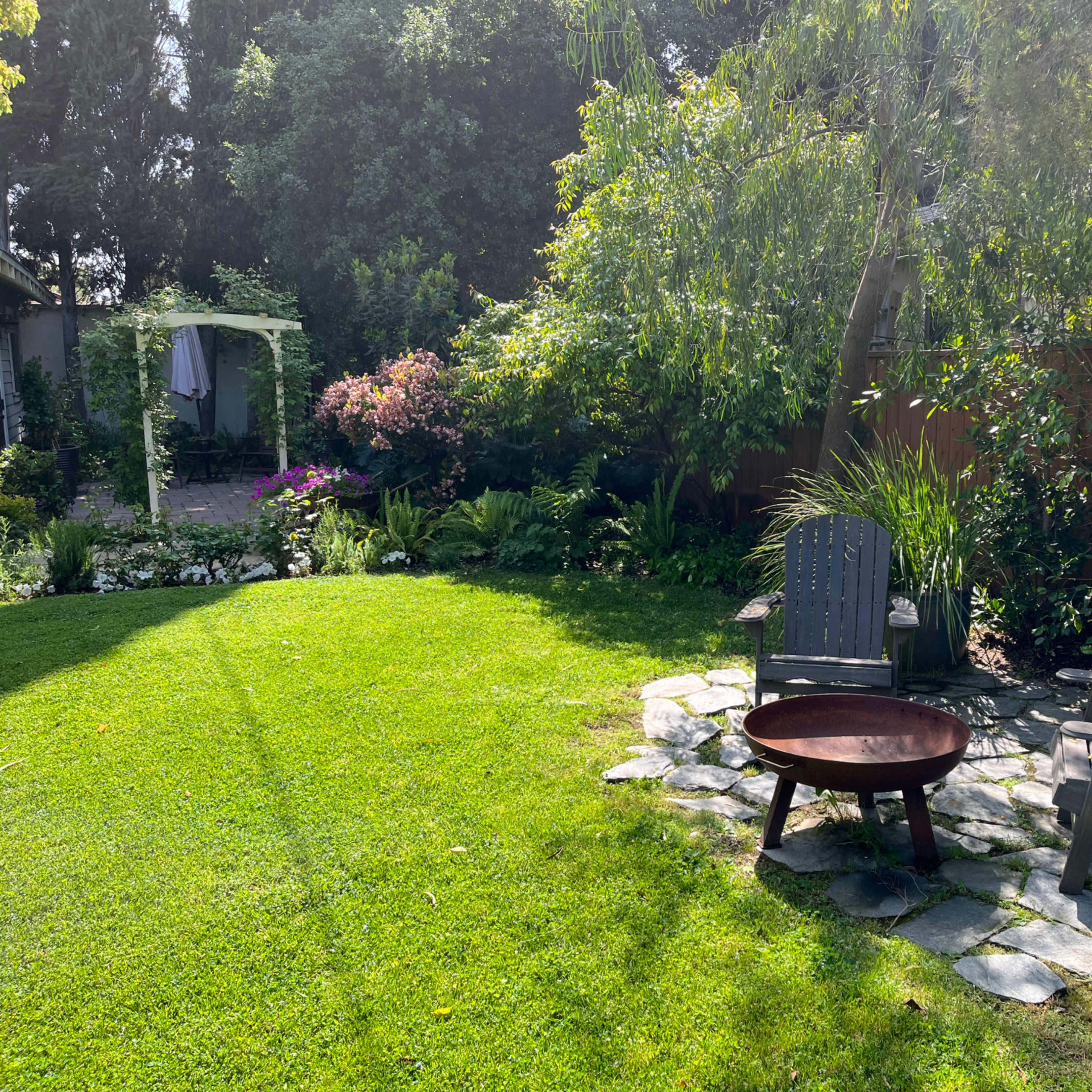 A well-maintained garden with a grassy area, stone pathway, and seating arrangement beside a fire pit.