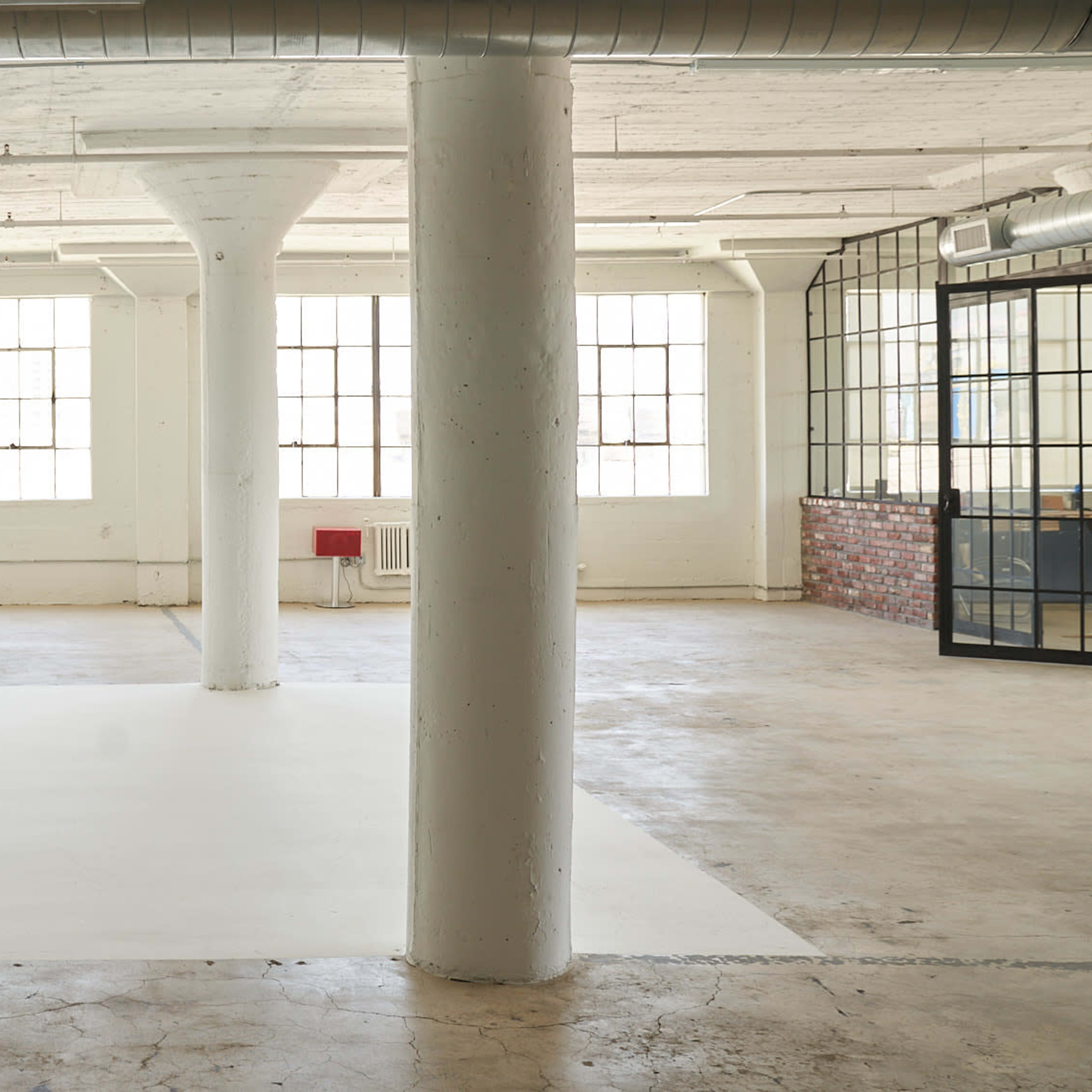 A spacious industrial-style studio with a curved white wall, large windows, and a table set with chairs on a concrete floor.