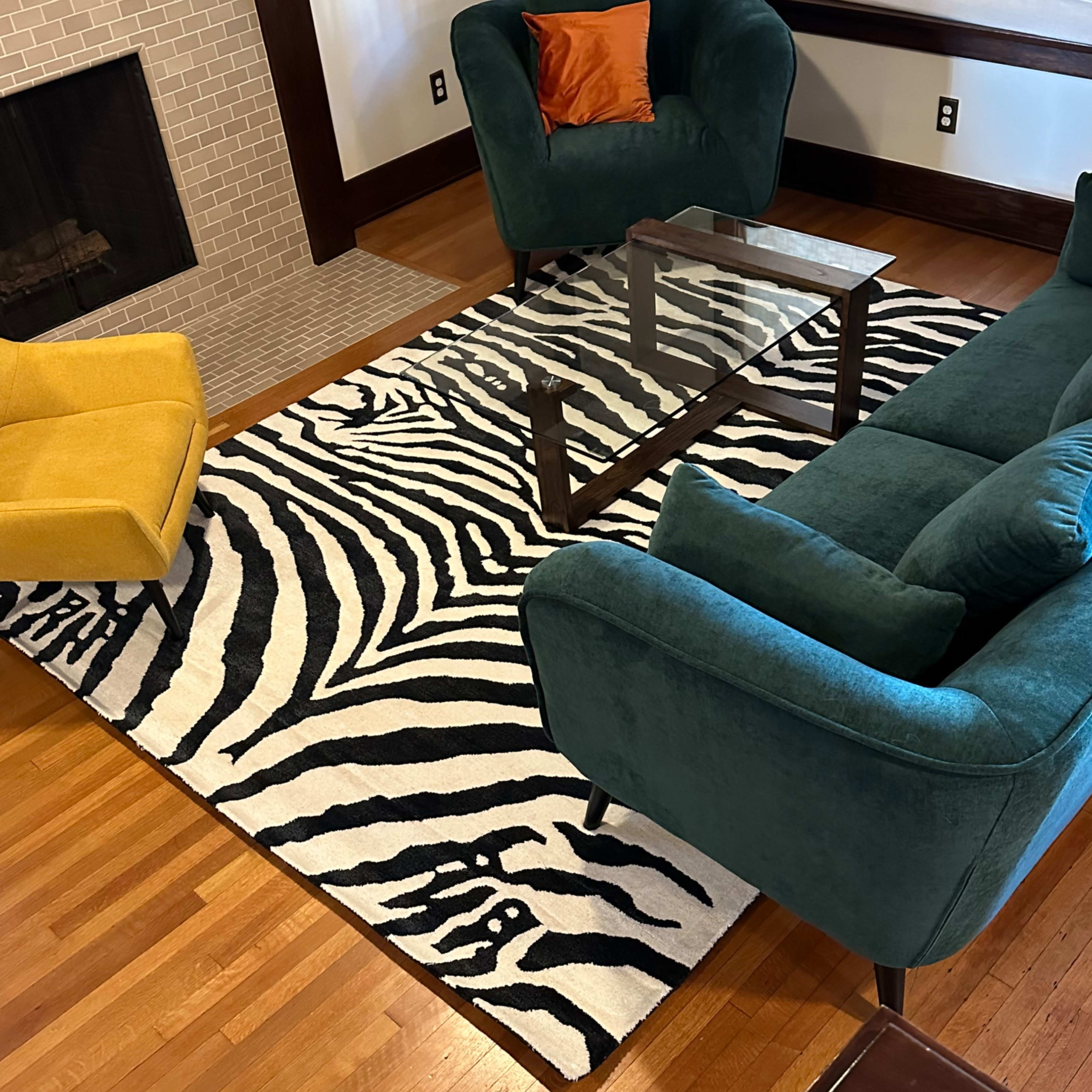 A living room with a zebra-striped rug, a glass coffee table, and a green sofa set, alongside a yellow accent chair, all placed on hardwood flooring.