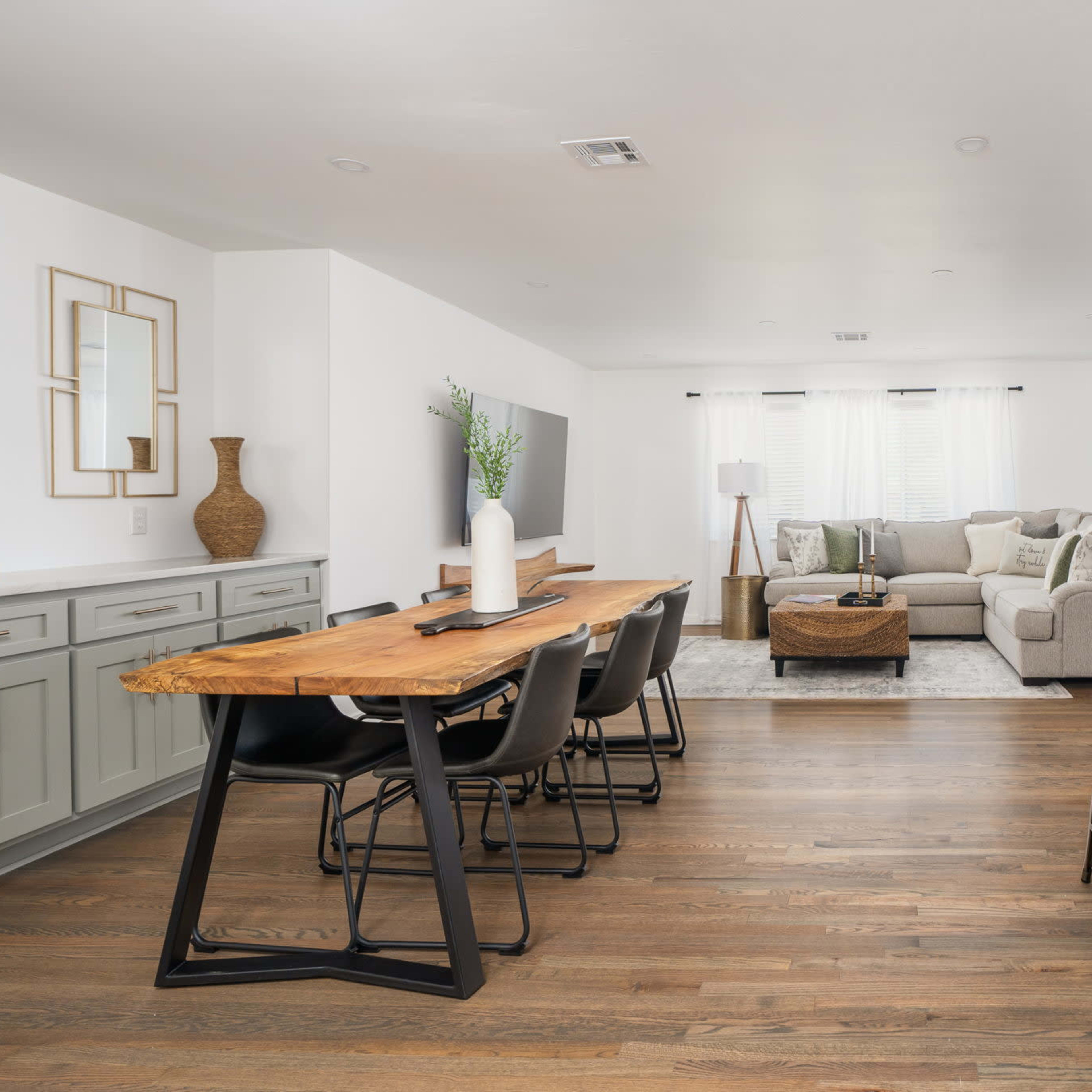 A modern open-concept living space featuring a dining area with a wooden table and black chairs, a cozy seating area with a light gray sofa, and a kitchen with bar stools.