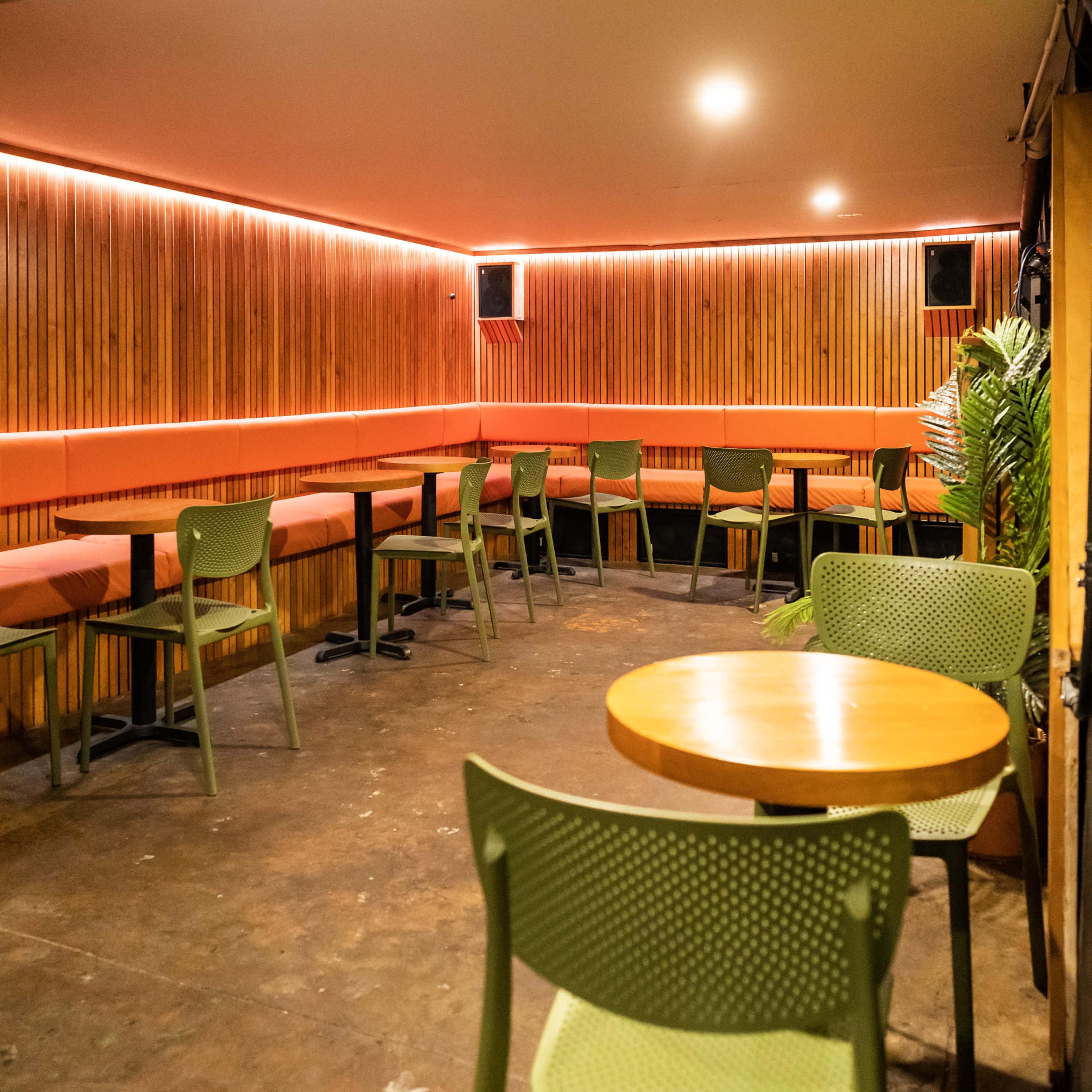 A sparsely furnished interior of a modern café with wooden paneling, minimalist green chairs, and warm orange lighting.
