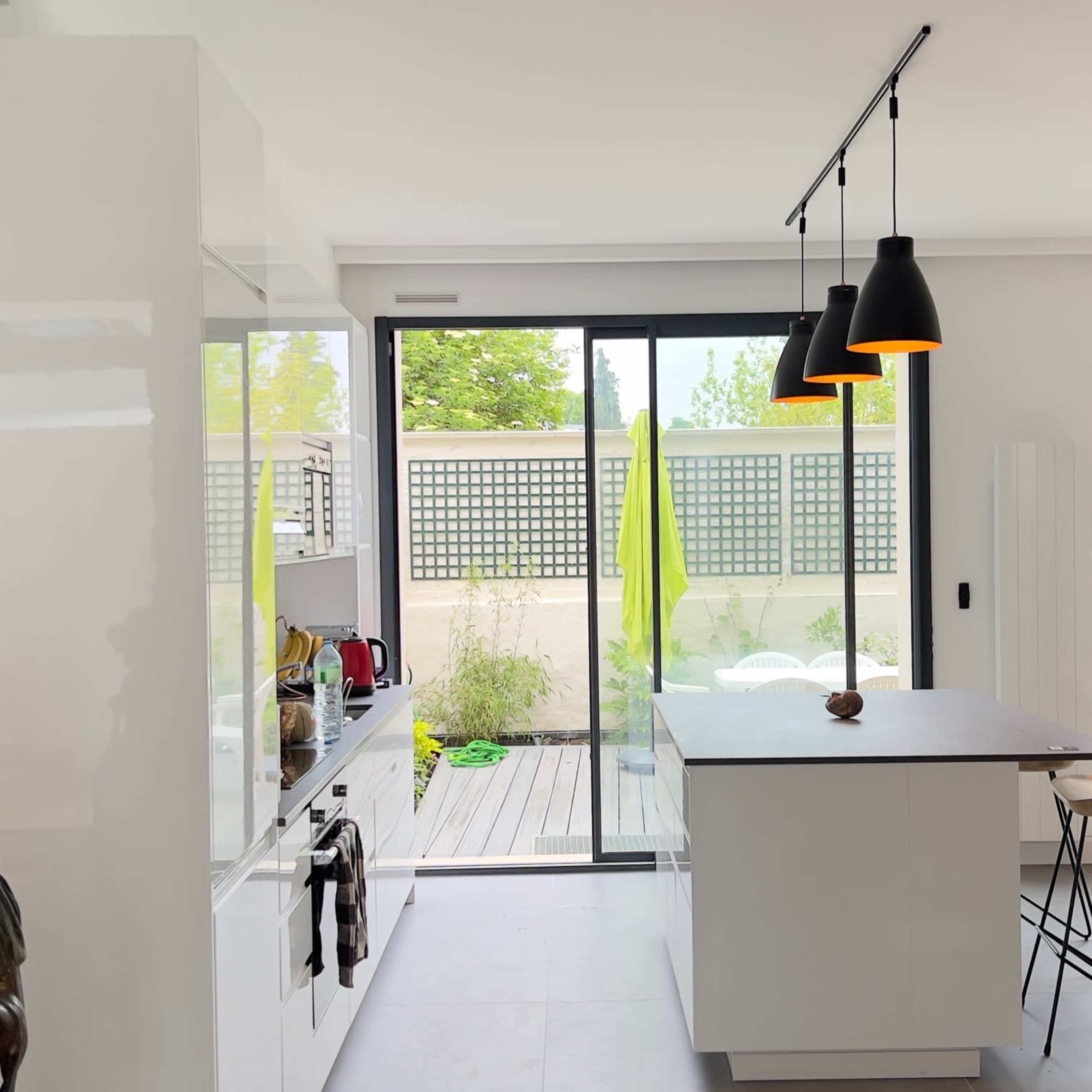 A modern kitchen with white cabinetry, an island with a black countertop, and large glass doors leading to an outdoor area.