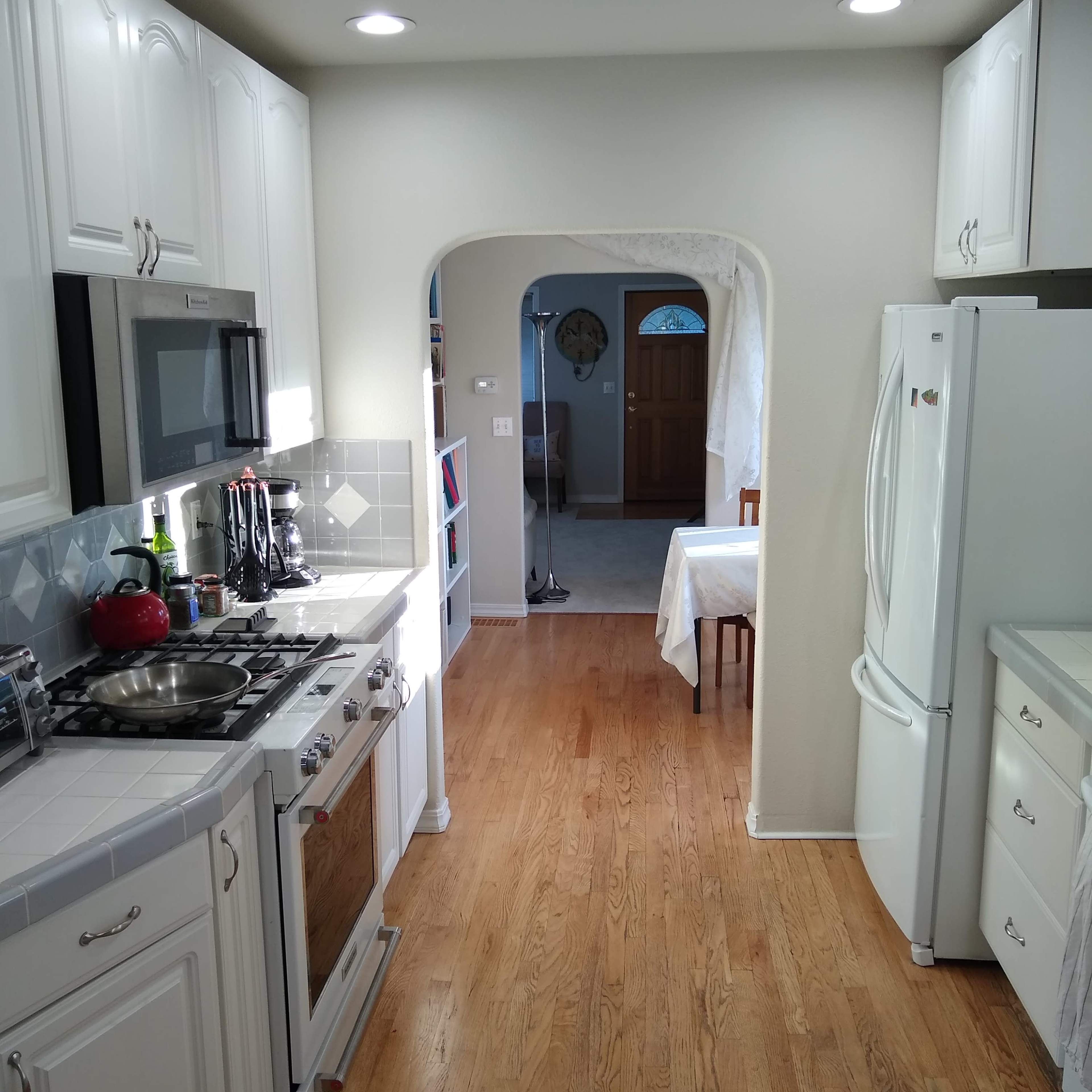 A tidy kitchen with white cabinetry and stainless steel appliances, extending into a hallway that leads to a dining area and an entrance door.