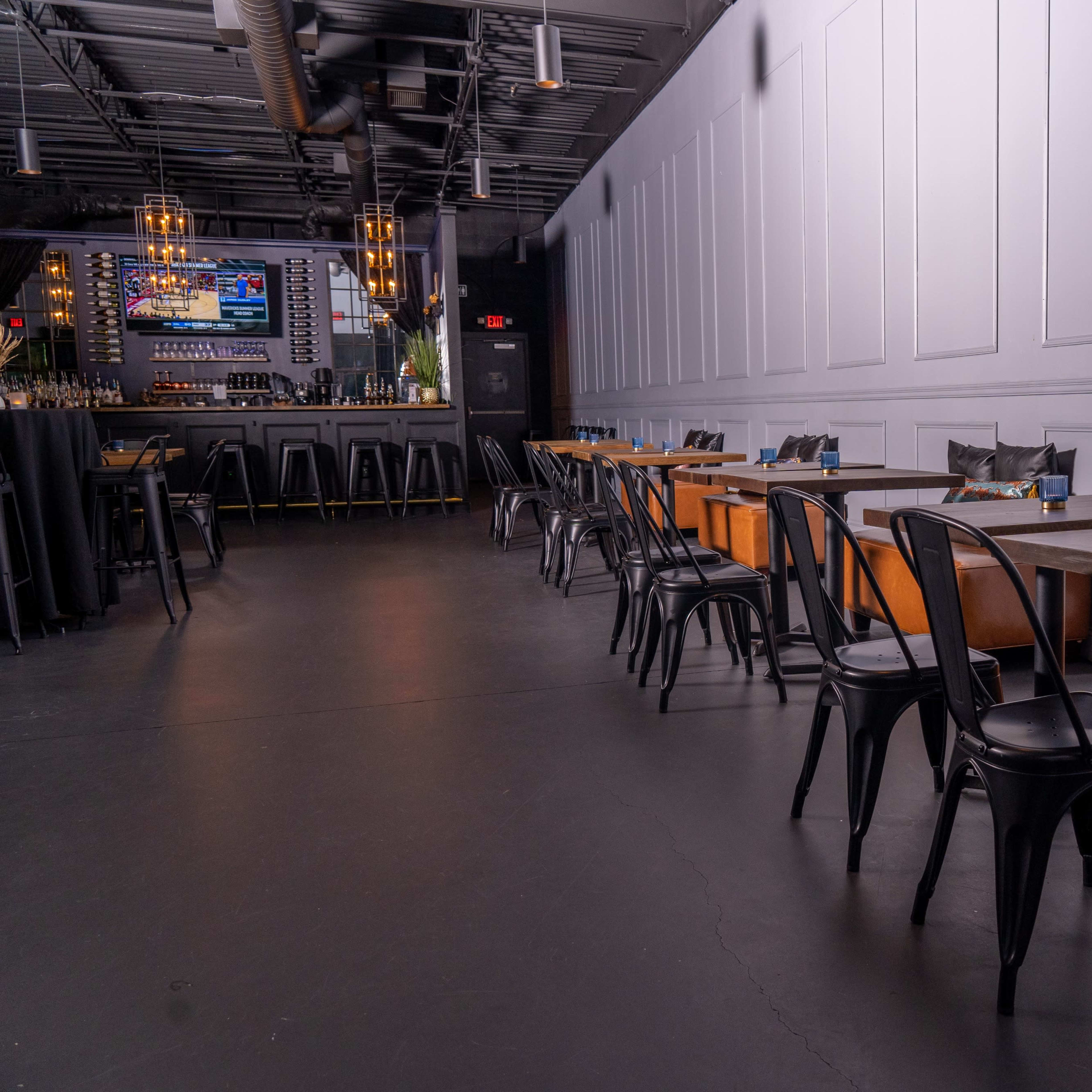 A modern restaurant interior featuring black metal chairs, dark wooden tables, and cozy leather banquettes along the walls.