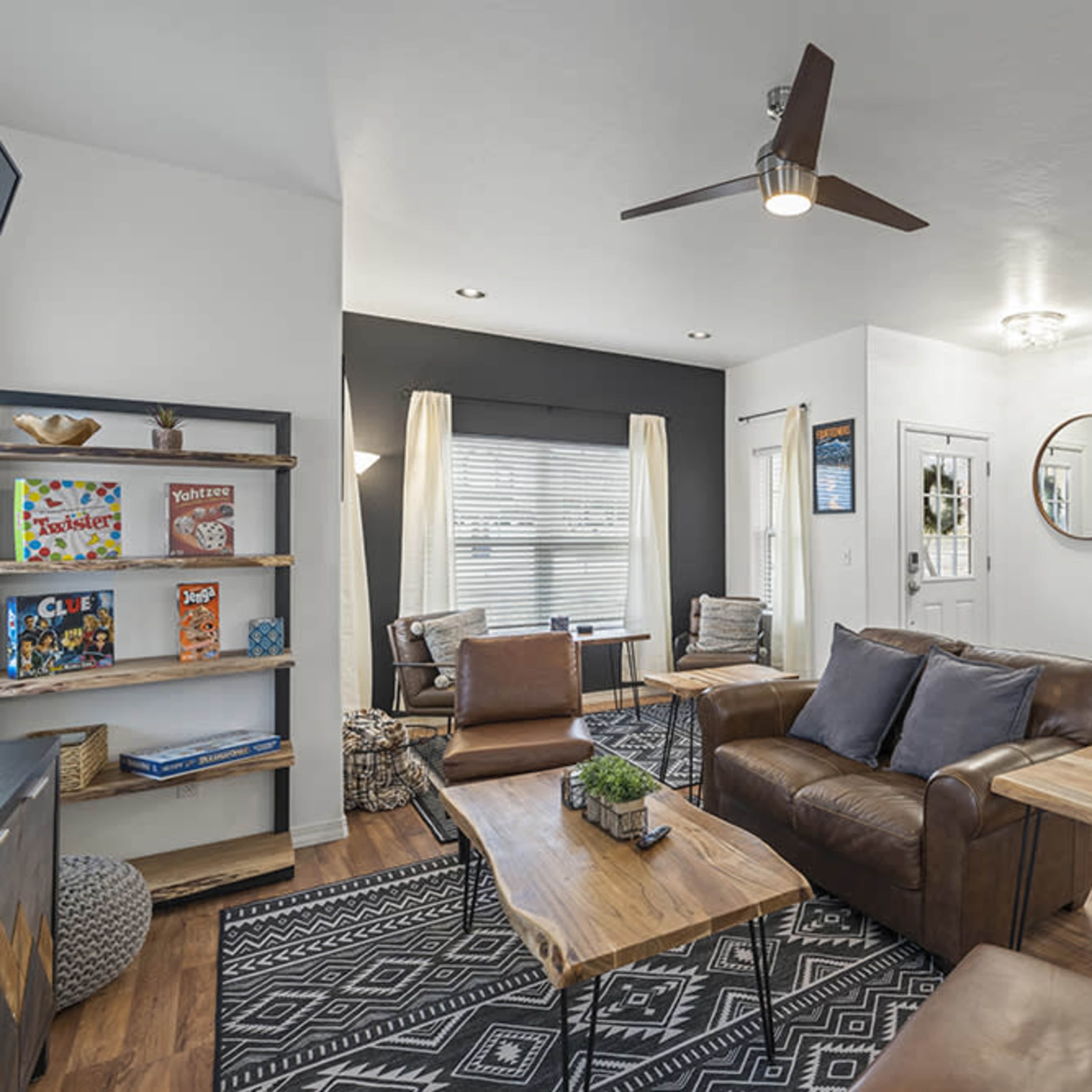 A modern living room featuring leather sofas, a wooden coffee table, and a shelf with magazines, set against a backdrop of neutral-colored walls and a patterned rug.