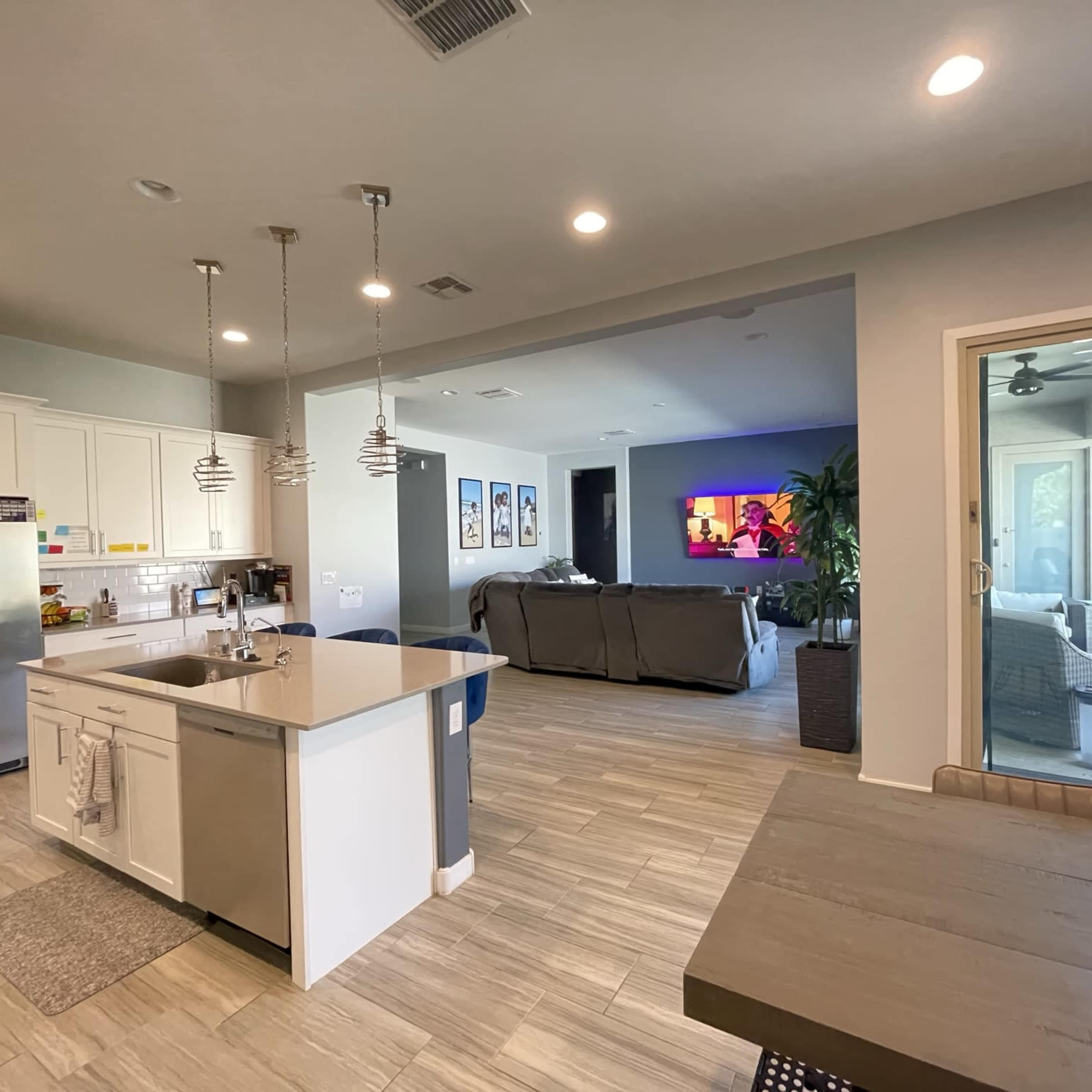 A modern kitchen with an island, open to a living area featuring a large couch and a wall-mounted TV.