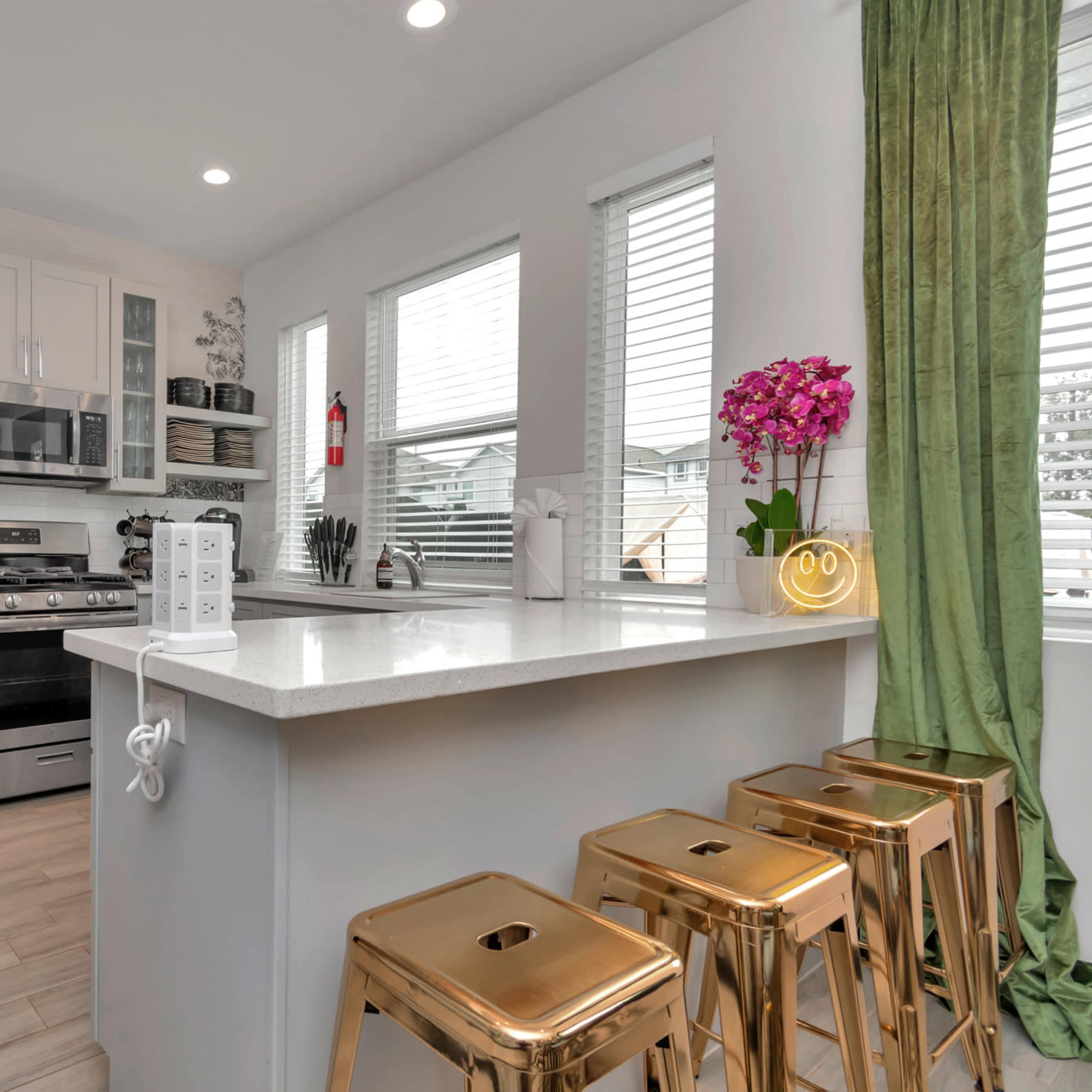 A modern kitchen features stainless steel appliances, white cabinetry, and a breakfast bar with three gold stools.