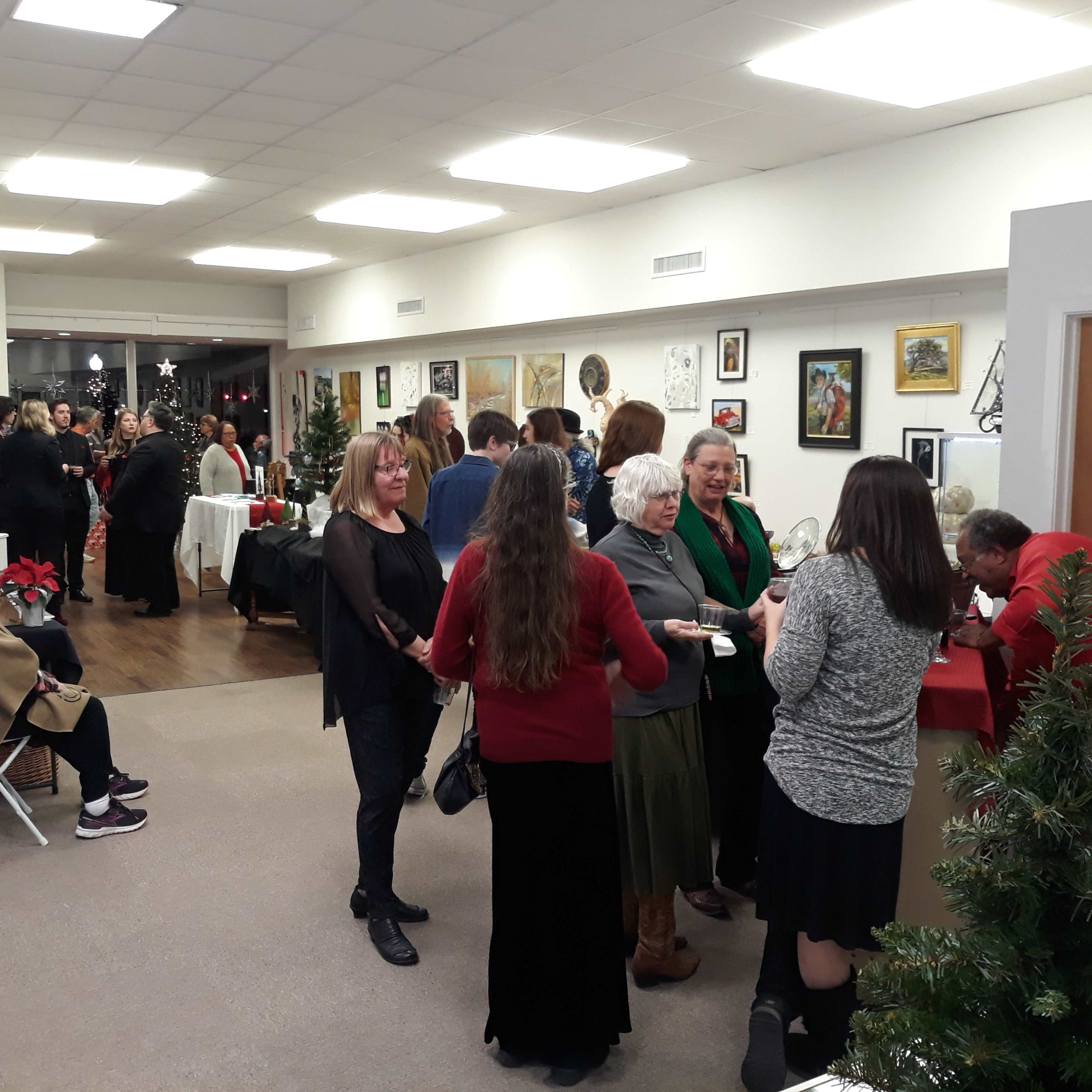 A group of people gather at an art gallery event, engaging in conversation while refreshments are served.