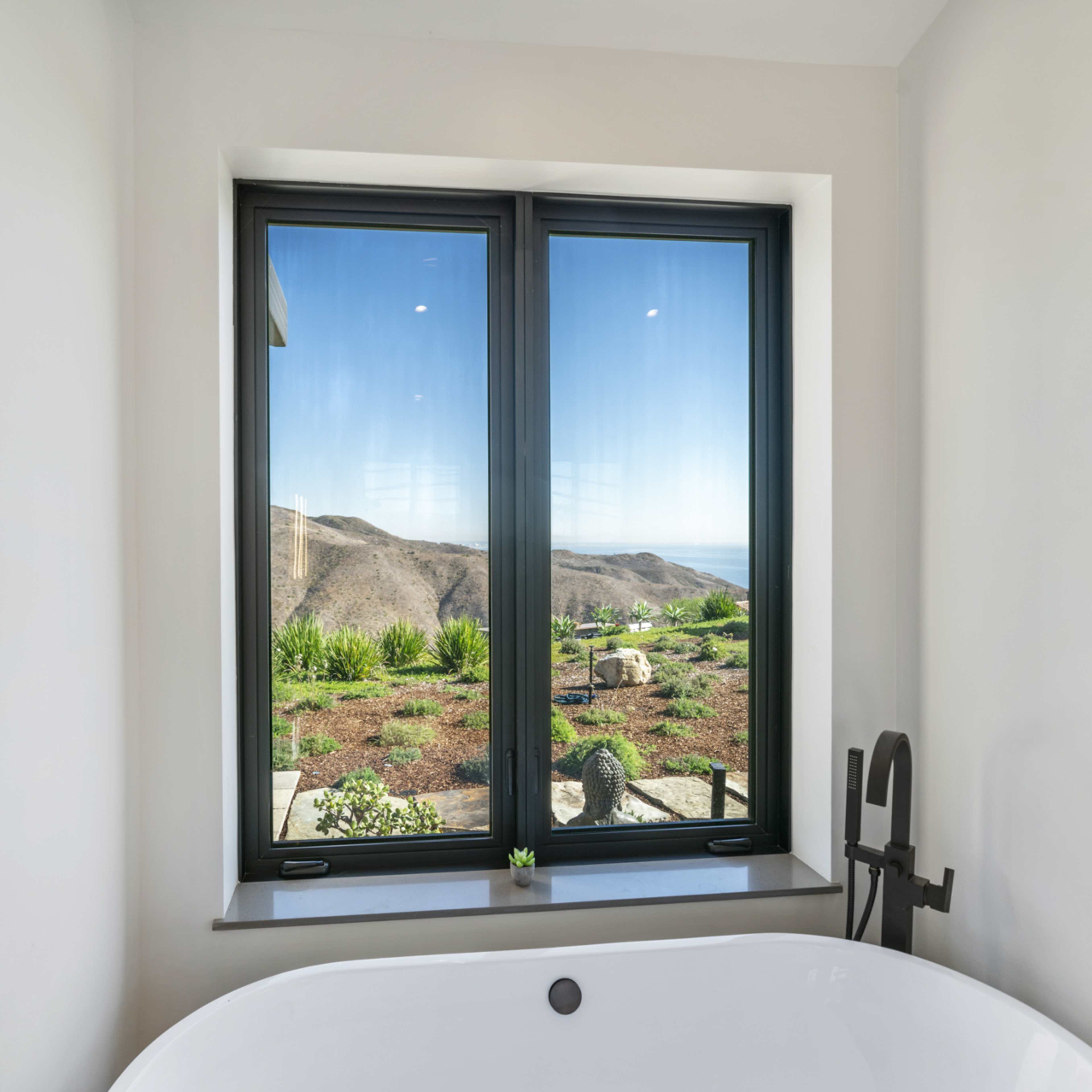A modern bathroom features a freestanding bathtub beside a large window overlooking a mountainous landscape.