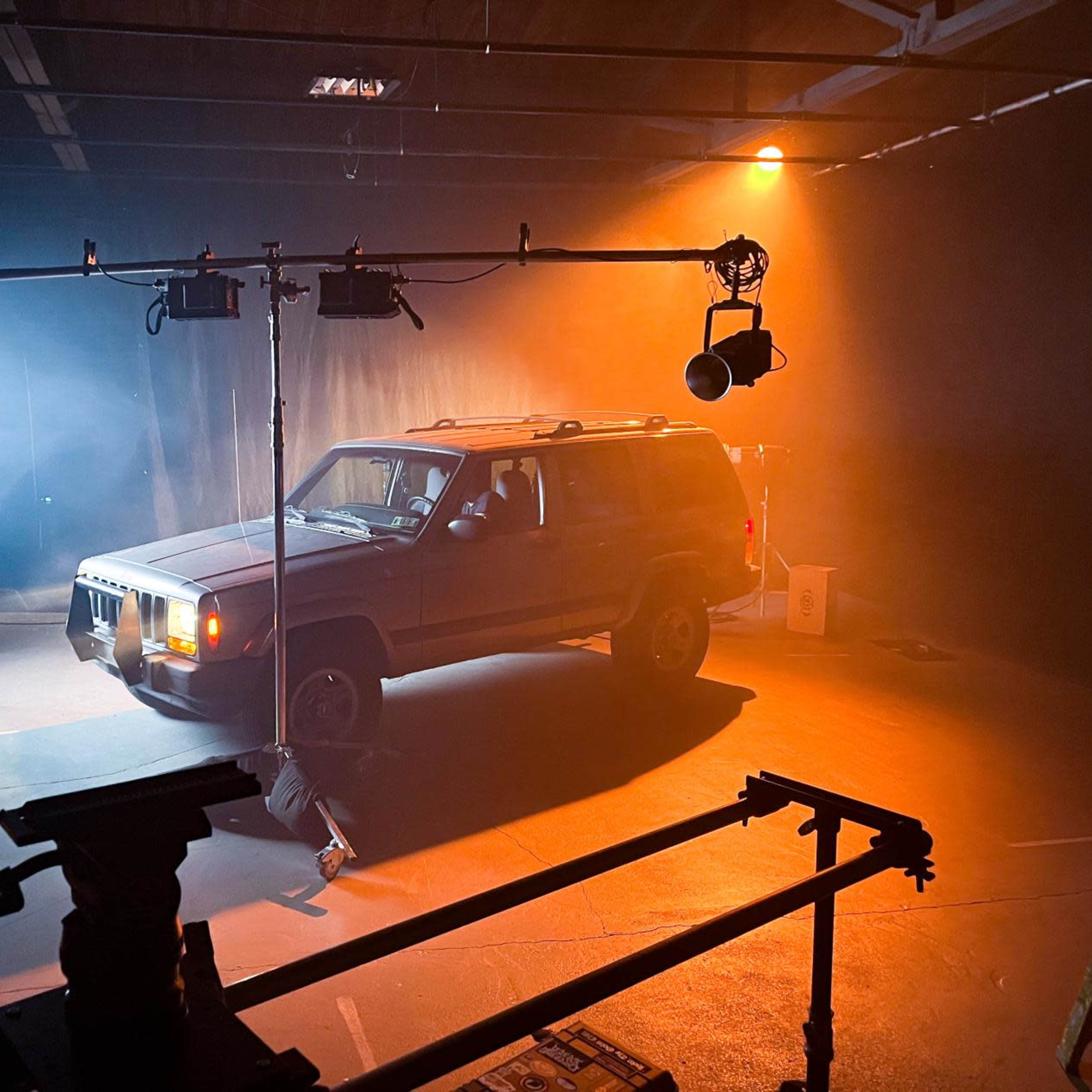 A parked SUV is illuminated by stage lighting in a dimly lit studio environment.