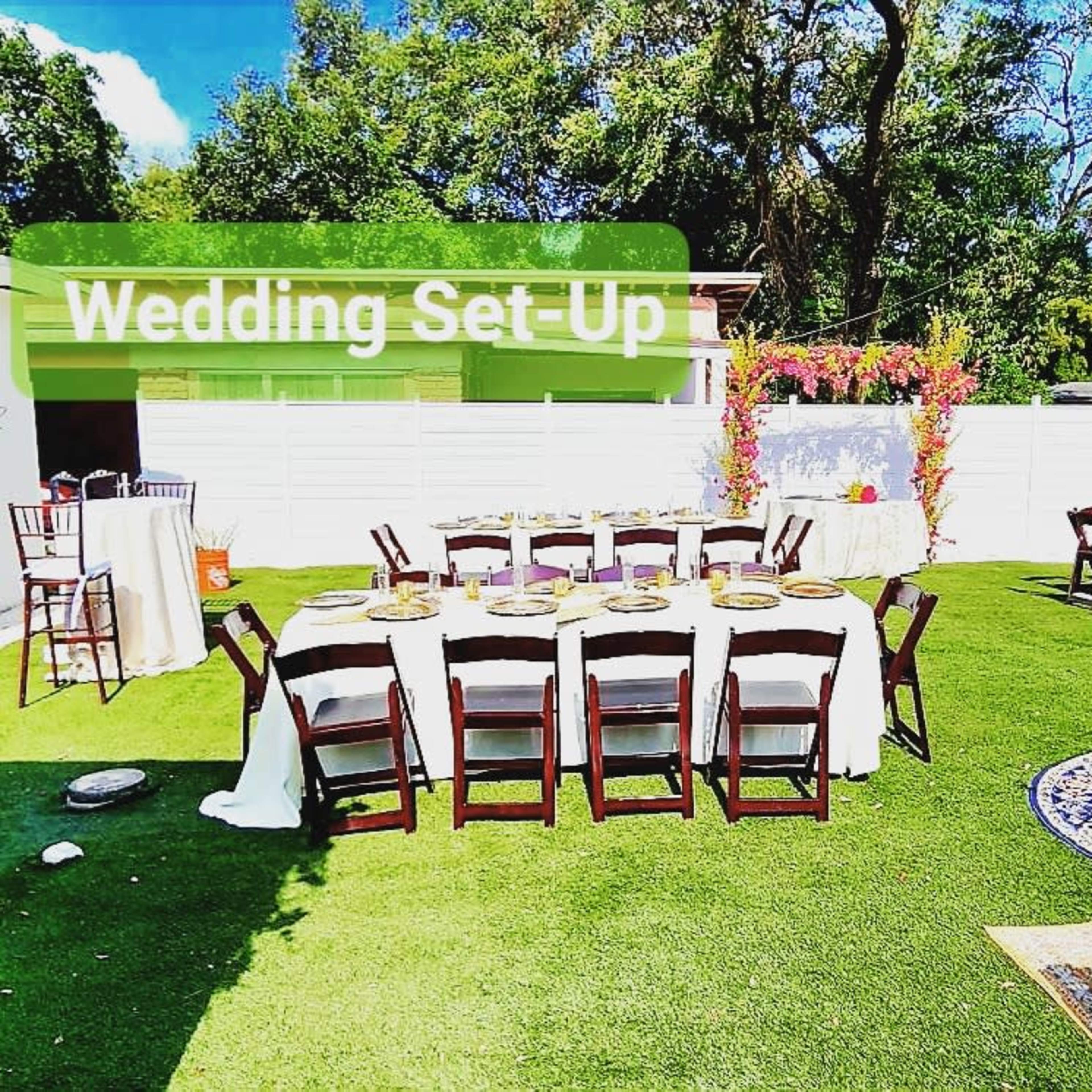 An outdoor wedding setup with tables, chairs, and a floral arch in a grassy area.