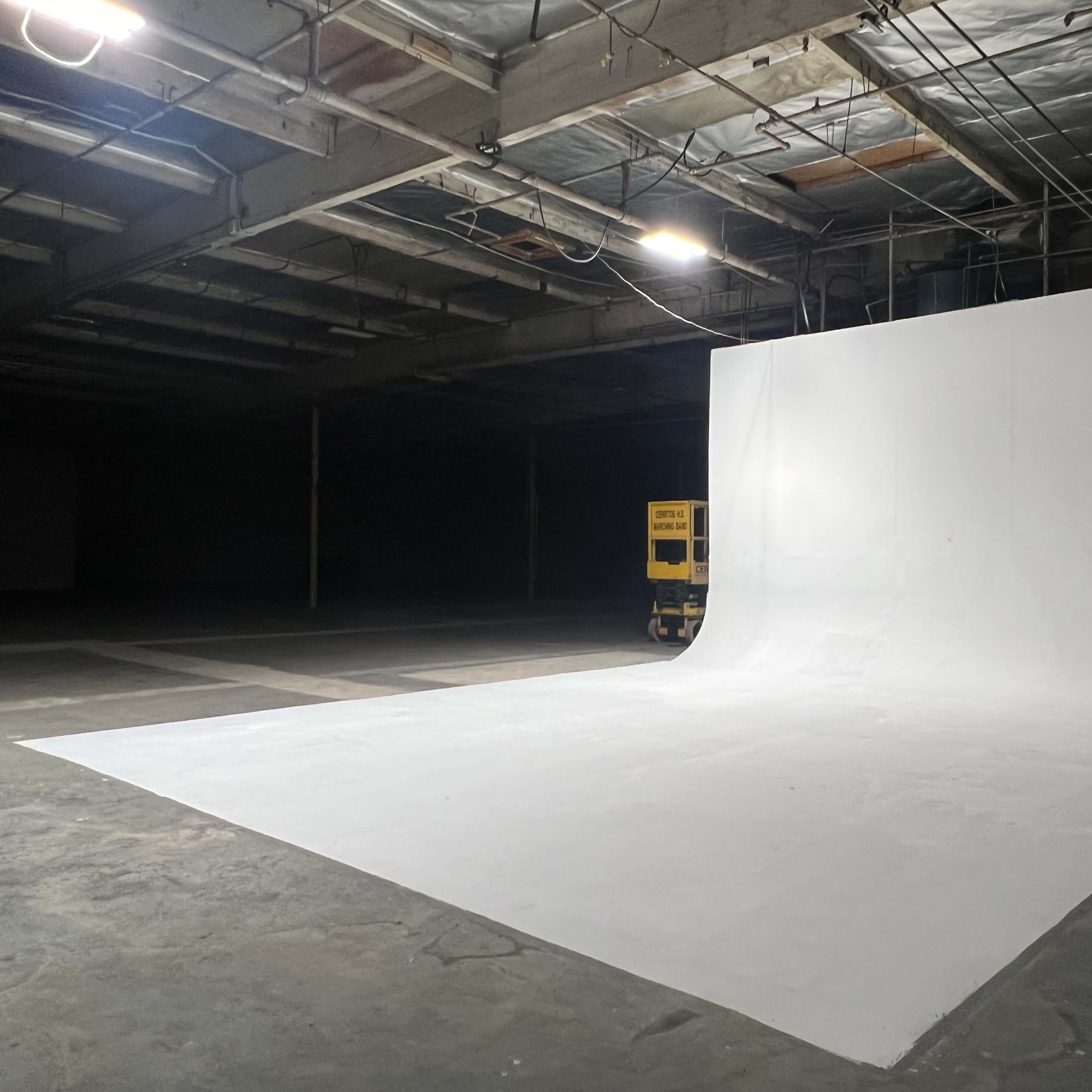 A large, empty studio space with a smooth white backdrop and concrete floor, illuminated by overhead lights.