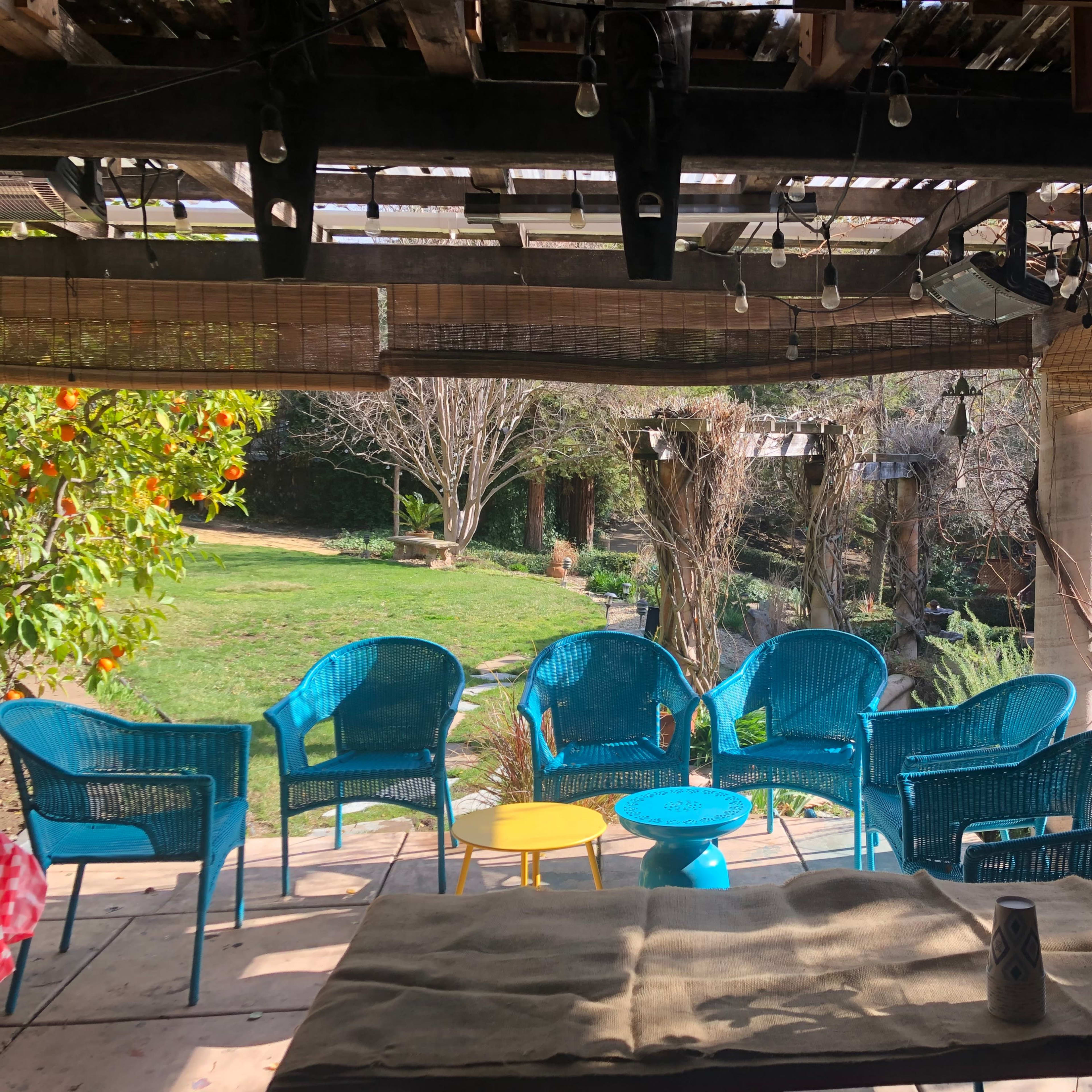 A cozy outdoor seating area with turquoise chairs and a small round yellow table, surrounded by greenery and trees.