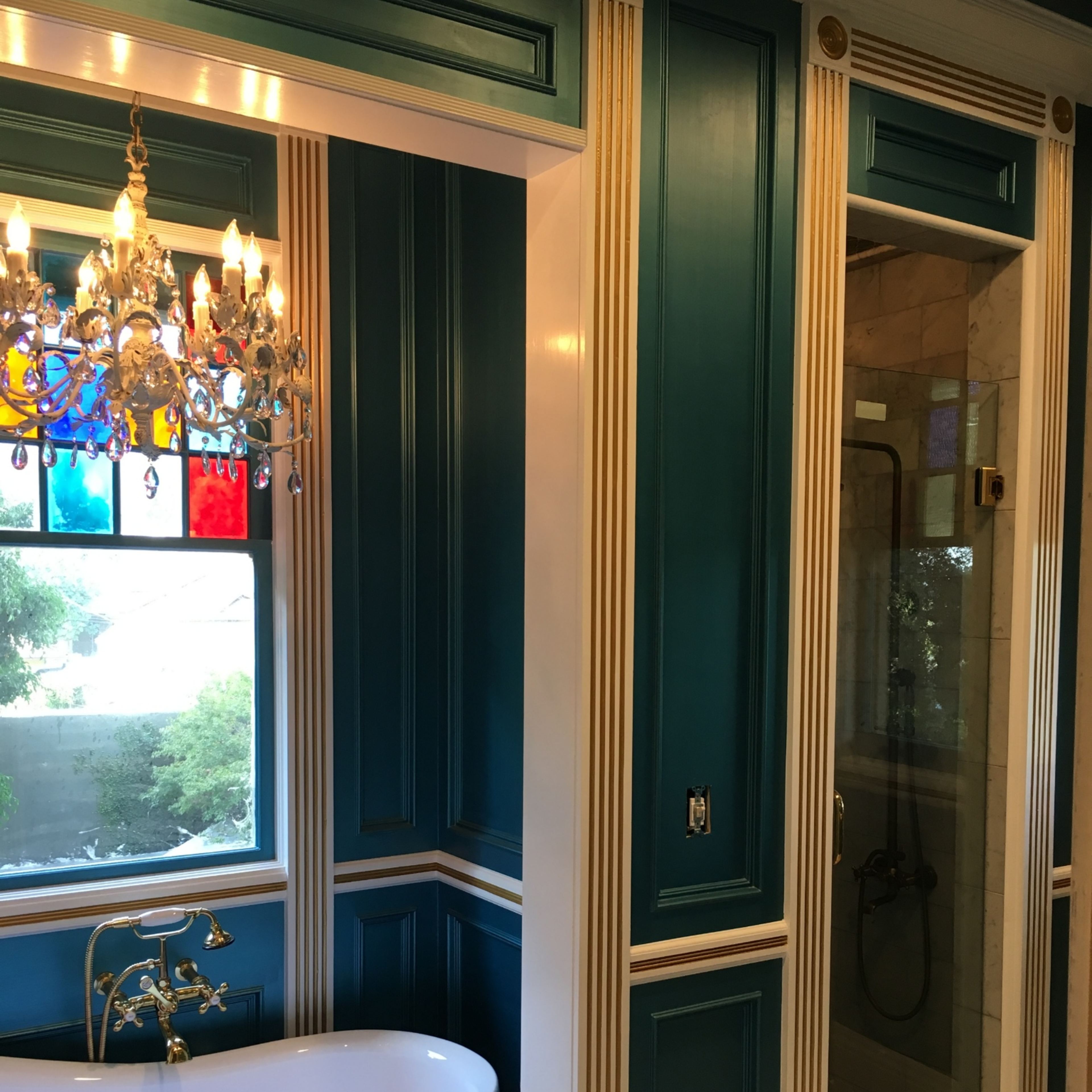 A luxurious bathroom with a freestanding tub, a decorative chandelier, and a glass shower enclosure set against blue and white paneled walls.